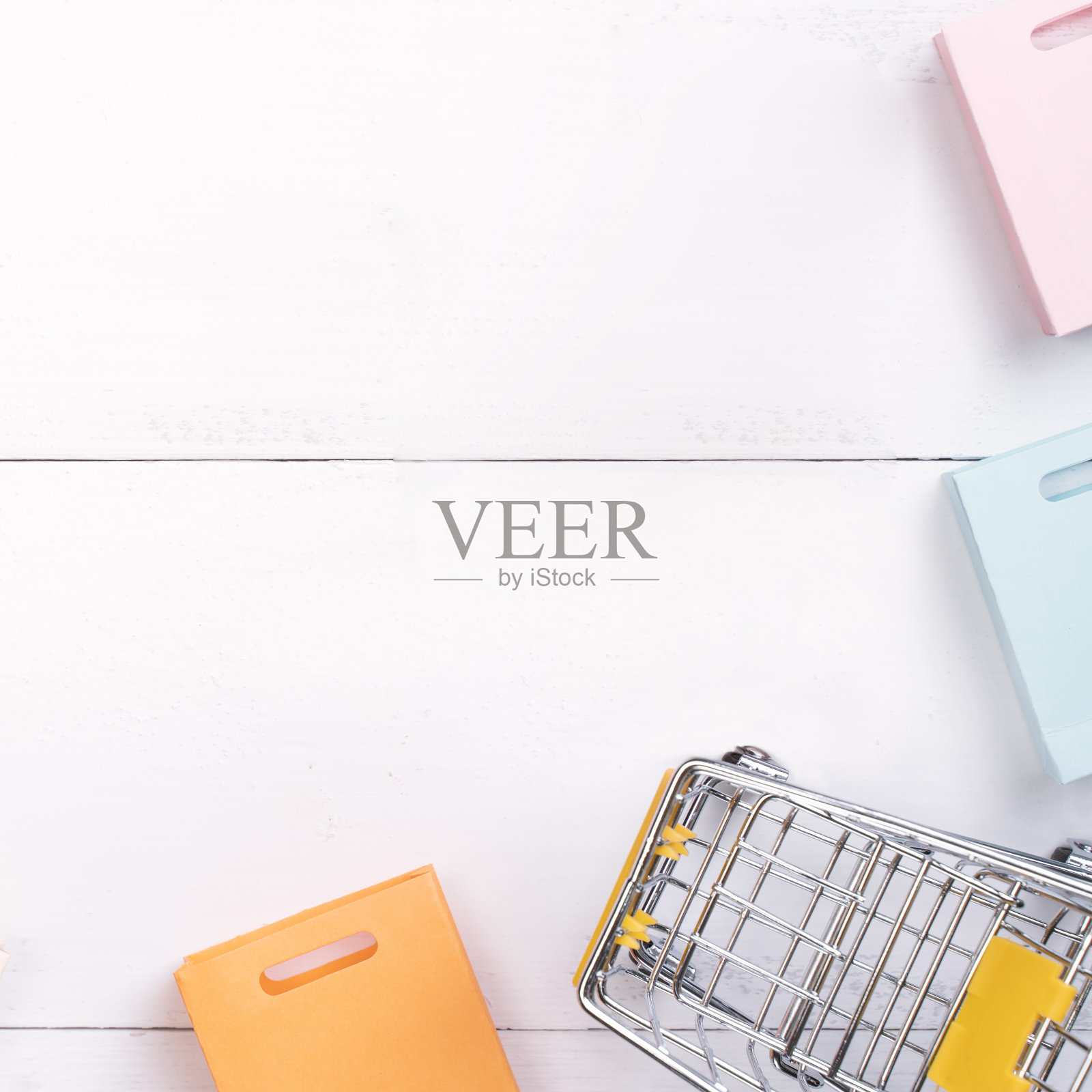 抽象的设计元素，年度销售，购物季节的概念，小手推车与彩色纸袋在白色木制桌子的背景。照片摄影图片