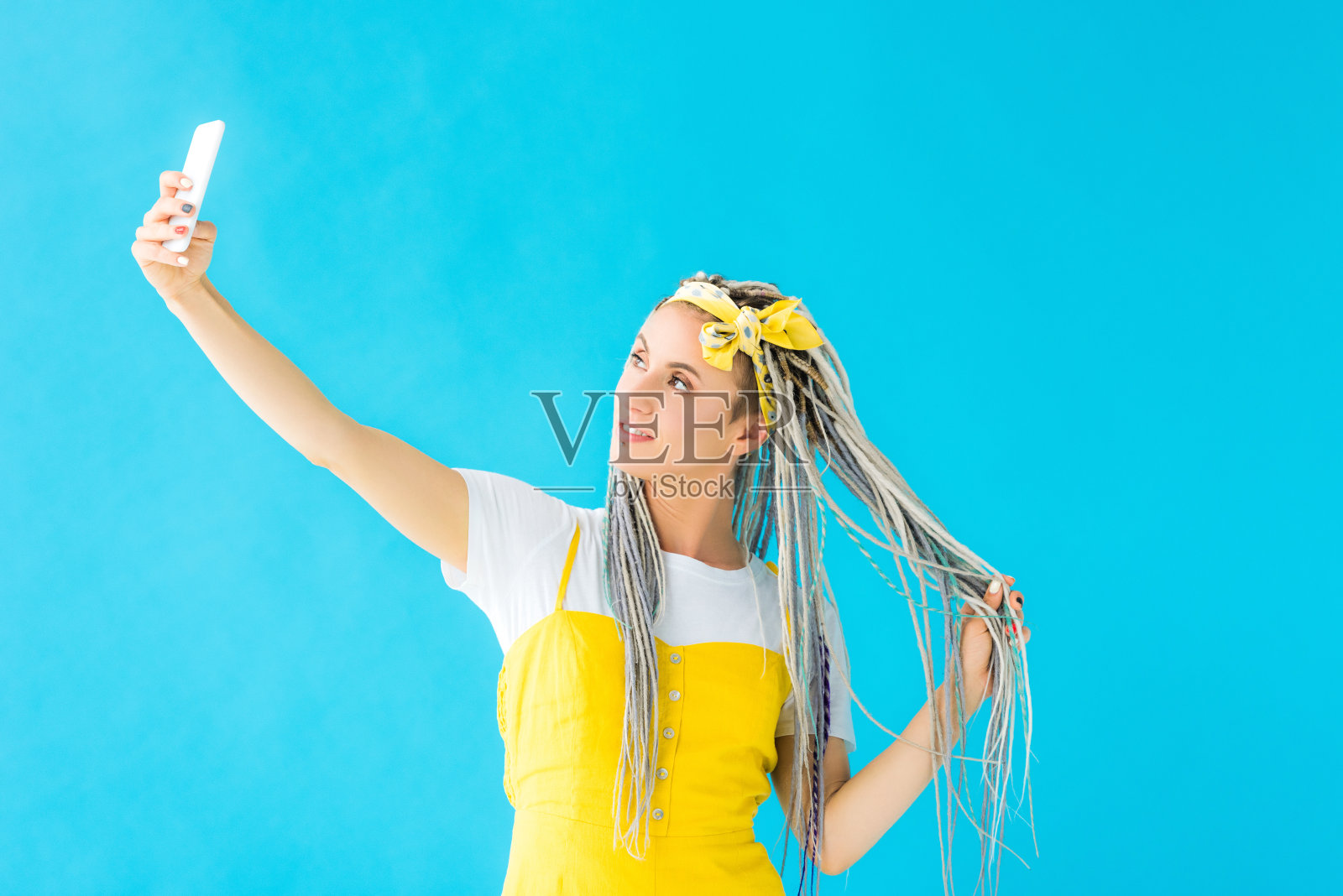 梳着发辫的女孩在智能手机上自拍，绿松石色隔离照片摄影图片