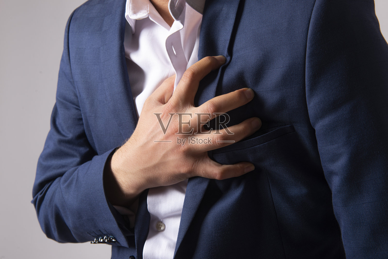 近距离拍摄的商人胸痛-心脏病发作-在灰色的背景下，年轻男子的腹部抱着他的心脏疼痛照片摄影图片