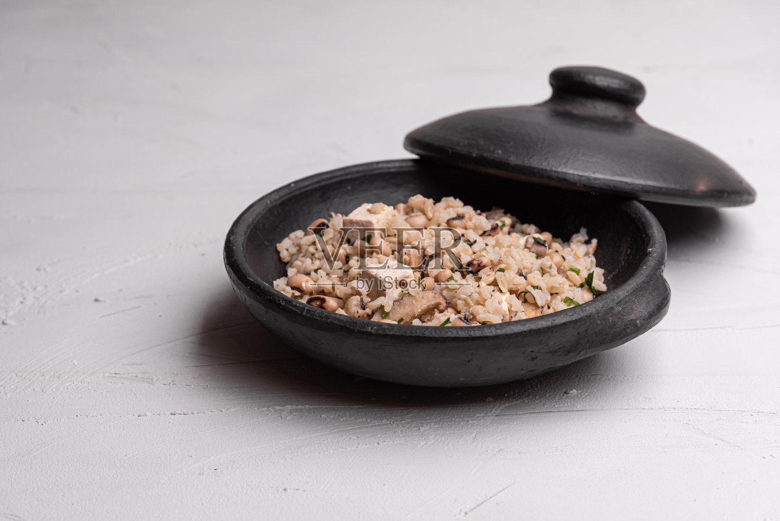 Baião de Dois -巴西传统食物-用香肠，凝乳奶酪，干牛肉和米饭在一个黑色的陶罐，在白色的背景。巴西东北部的典型菜肴。照片摄影图片