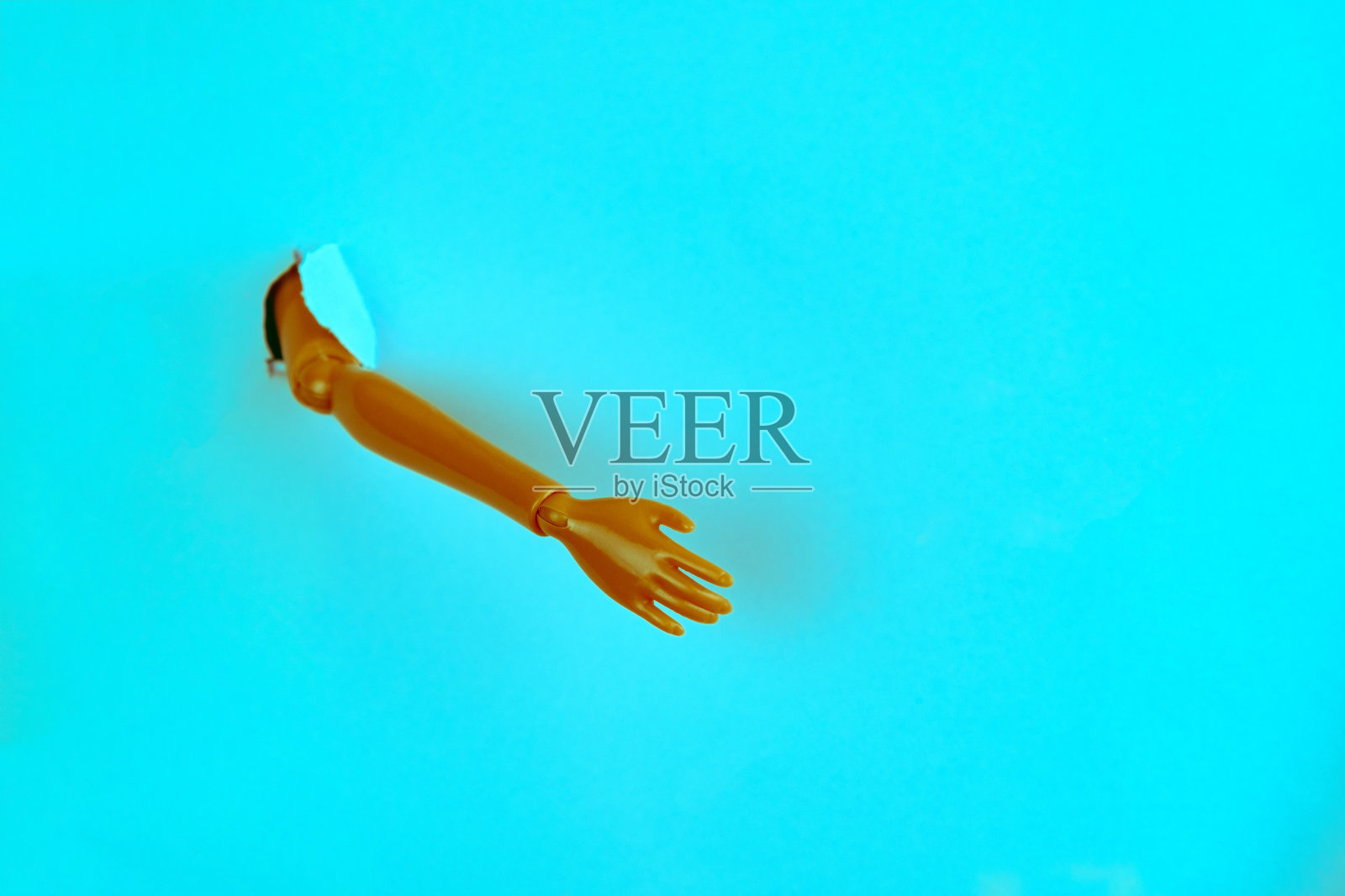 一个塑料娃娃的手突破破破的蓝色纸创意极简静物生活照片摄影图片