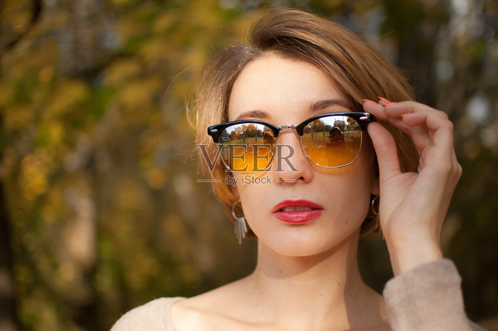 年轻美丽的女孩，一头短发，戴着镜面黄色太阳镜，在秋天的公园里，背靠着树叶的背景摆造型照片摄影图片