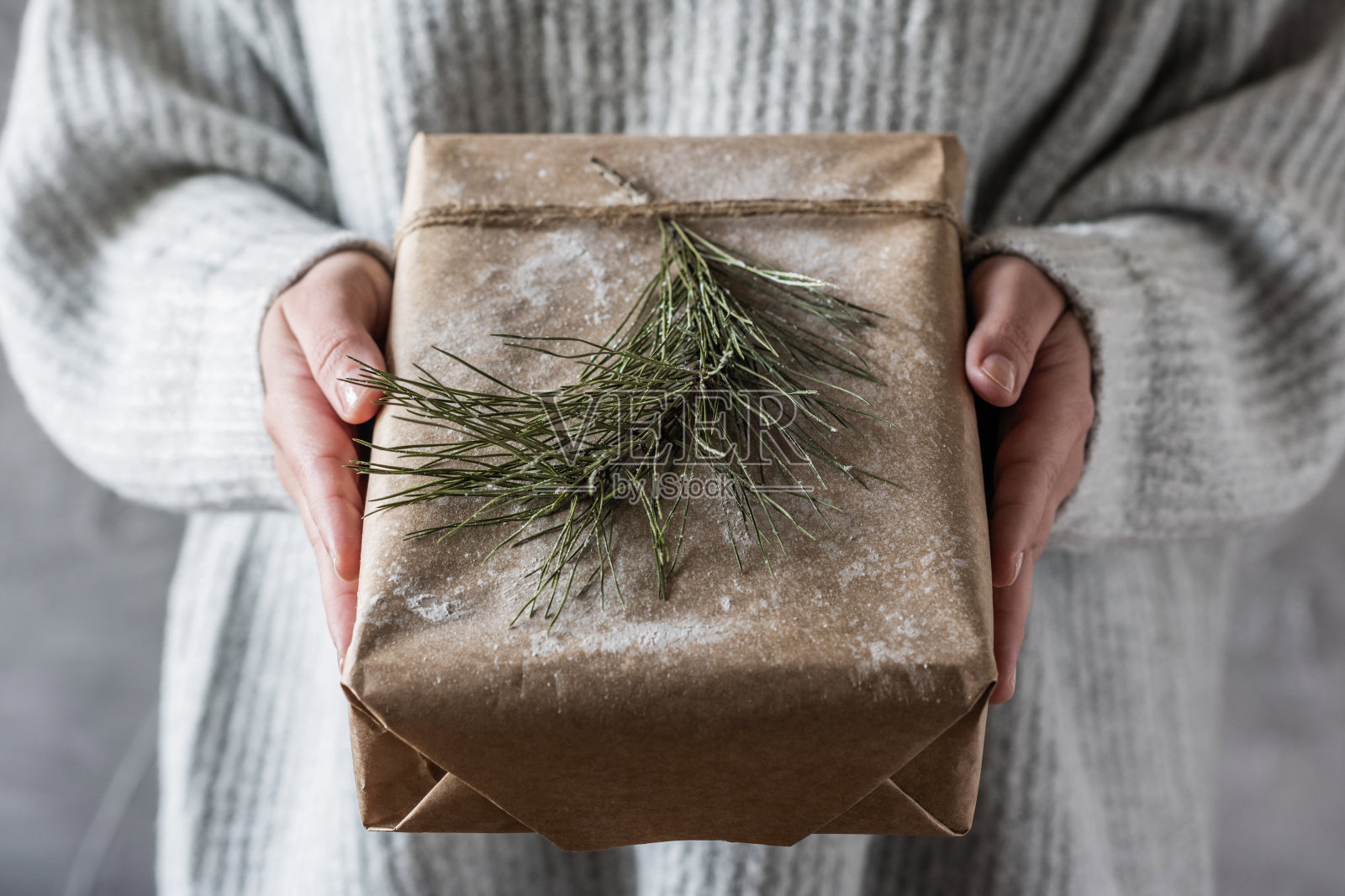 女孩在一个编织的冬天毛衣拿出一个大手制作的圣诞礼物盒牛皮纸和弓绳。DIY。概念照片摄影图片