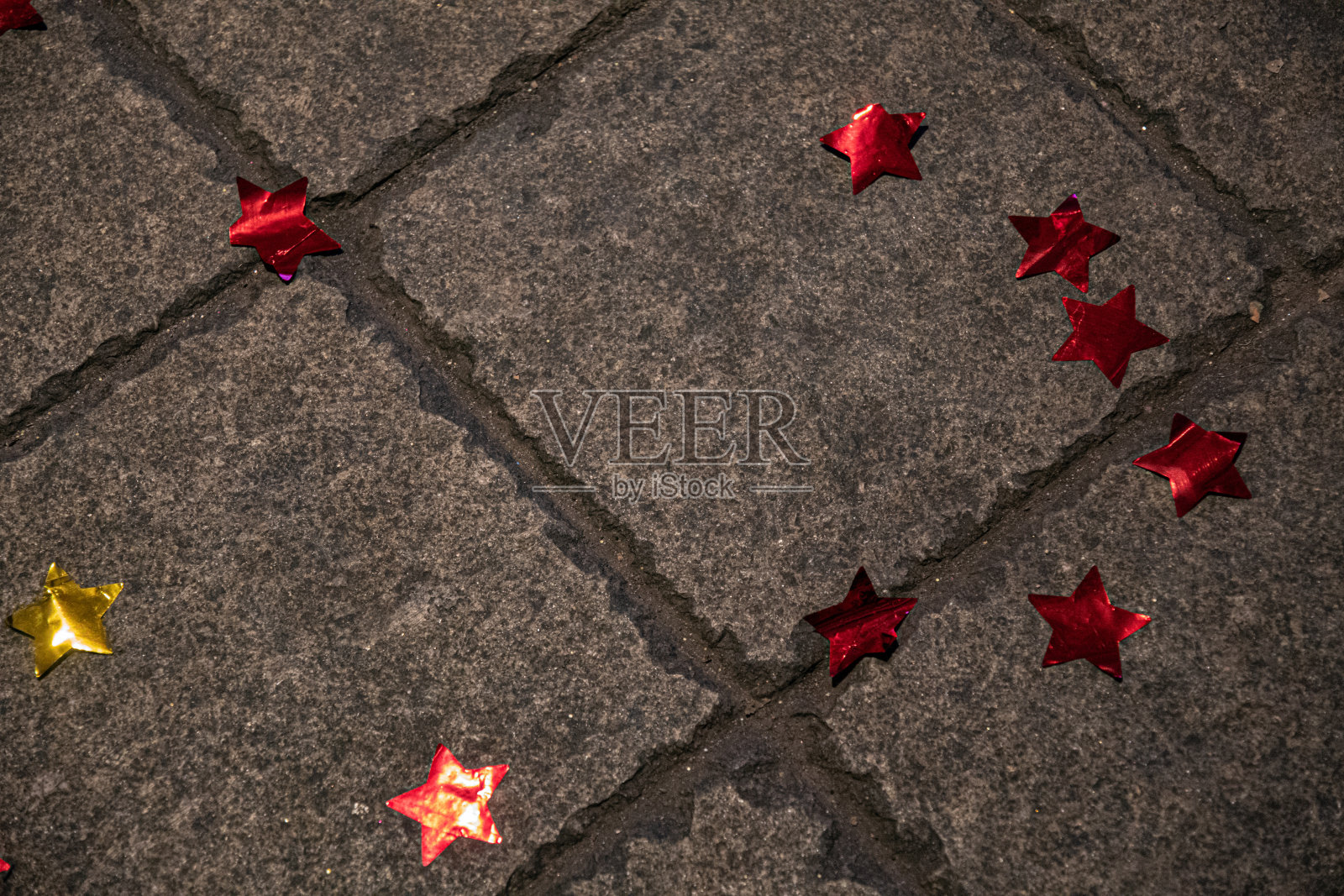 粗糙的石头表面铺着闪闪发光的星星。抽象背景与金色和红色箔星形装饰地面。生日聚会的主题。节日装饰照片摄影图片