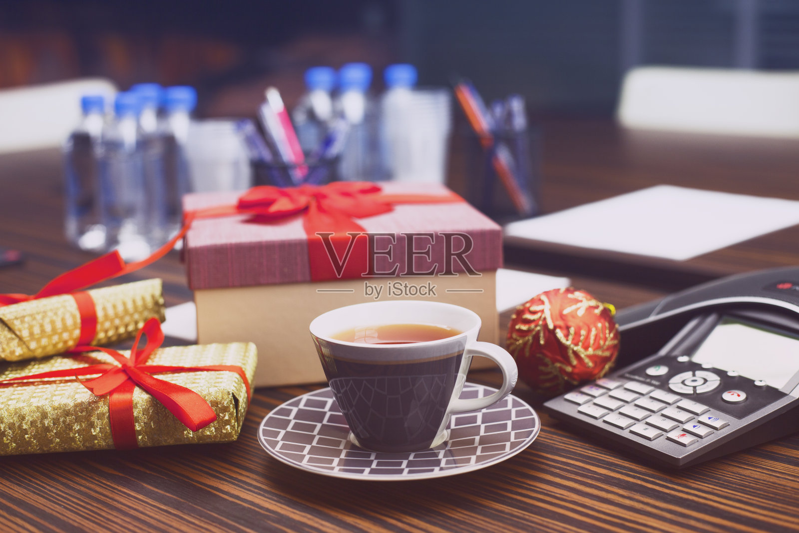 年轻的商人在办公室被礼物包围着。工作场所，一杯茶，笔记本电脑，ip电话和盒子。同事送的圣诞礼物。秘密圣诞老人办公室传统。新年的背景。照片摄影图片