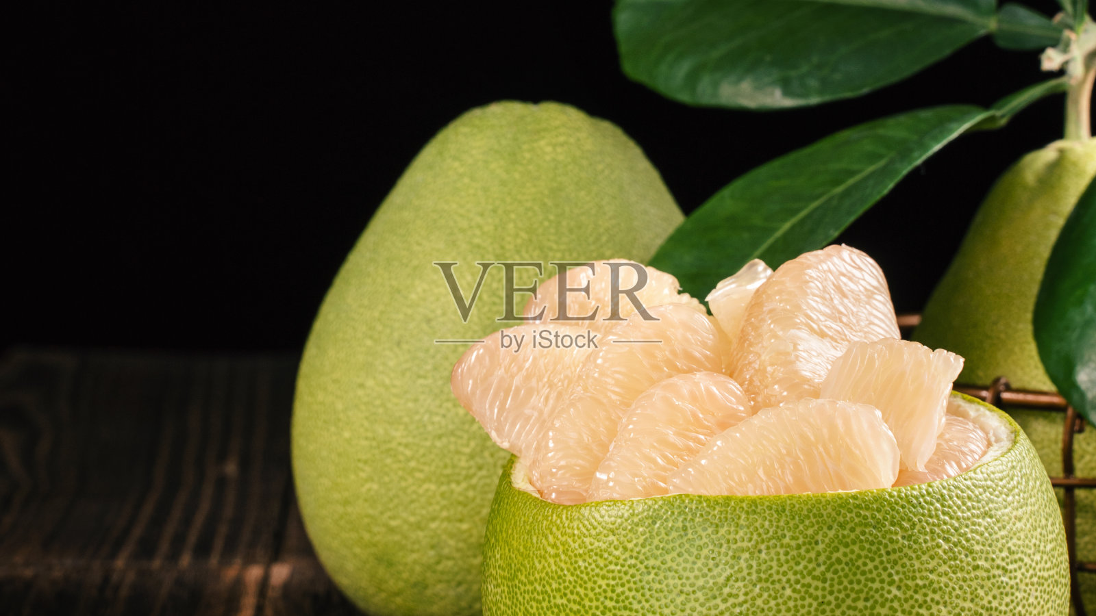 新鲜去皮柚子、葡萄柚、绿叶柚子放在深色木板桌上。中秋节附近的季节水果。照片摄影图片