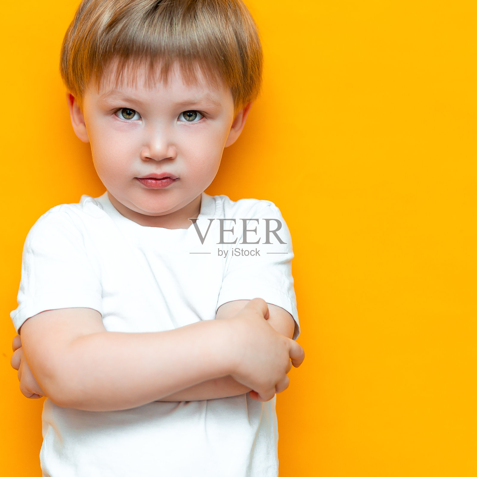 一个愤怒的小男孩，双臂交叉，孤立在黄色背景上。悲伤和不幸的孩子。沮丧蹒跚学步的小男孩照片摄影图片
