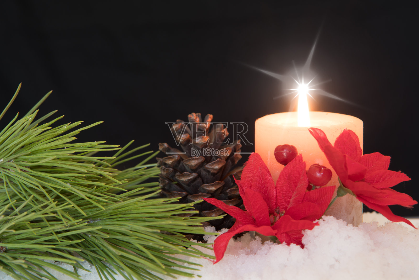 红色的一品红花与点燃的白色蜡烛，松针和松果在雪中。黑色圣诞背景与节日主题。照片摄影图片