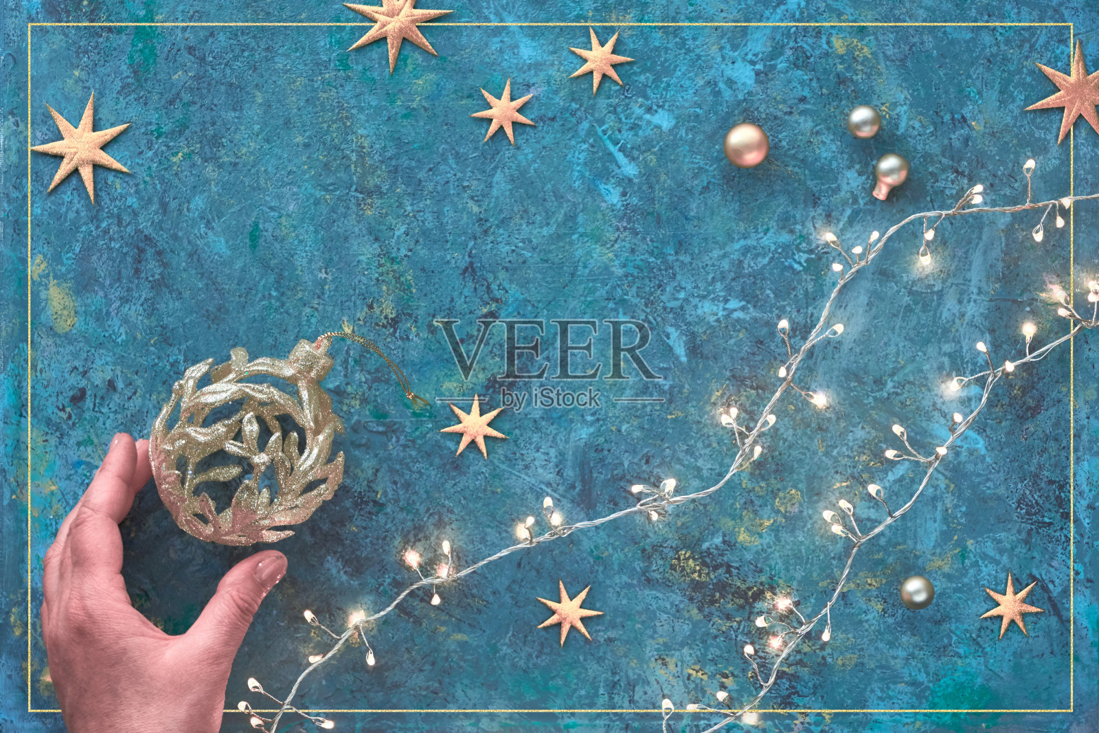 圣诞节或新年平铺背景在深色纹理板。俯视图平放在圣诞花环，金色的小饰物和星星。手持华丽的饰品。圣诞快乐，新年快乐!照片摄影图片