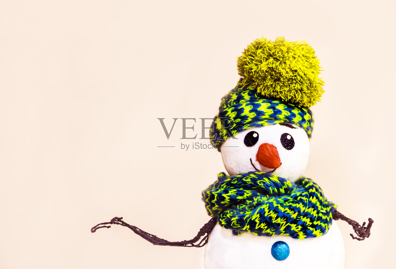 一个快乐的雪人的肖像，戴着淡绿色的帽子，脖子上围着一条围巾，在温暖的米黄色的背景，提供您的产品新年或圣诞节。照片摄影图片