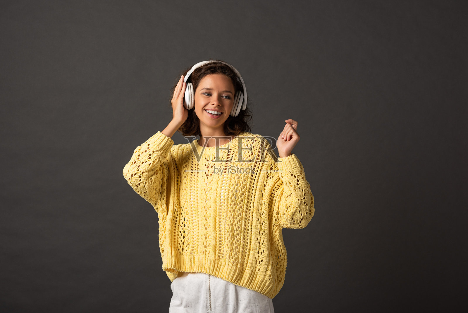 微笑卷曲的女人在黄色针织毛衣听音乐耳机在黑色的背景照片摄影图片