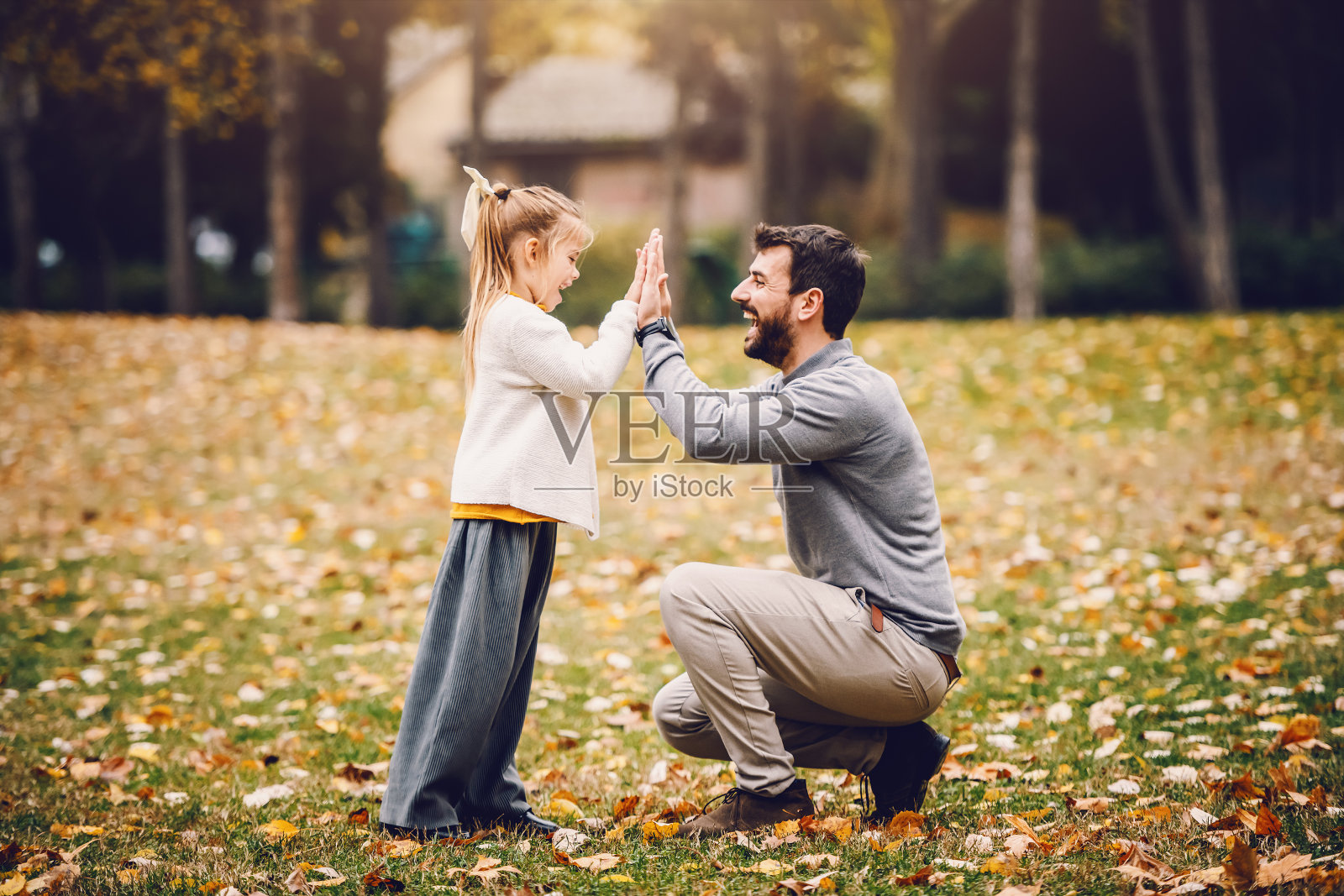 侧面的父亲和女儿在公园给在公园击掌。秋天的时间。照片摄影图片