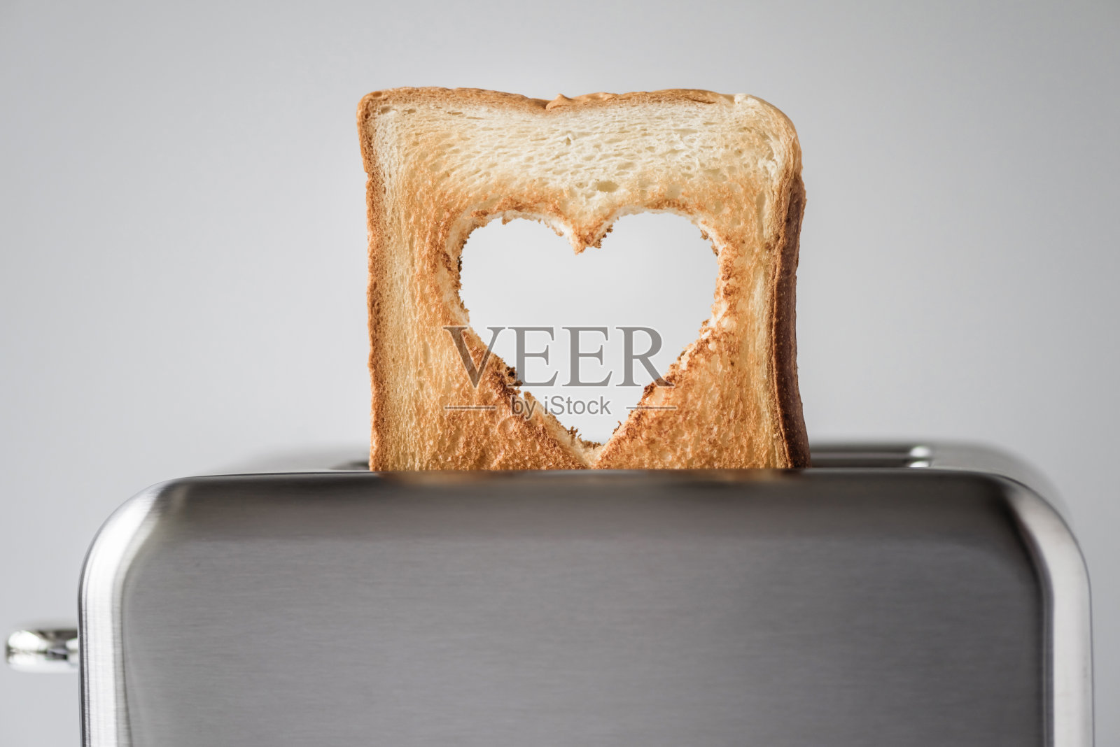 在烤面包机上烤出心形的面包。准备情人节早餐。爱的象征。概念照片摄影图片