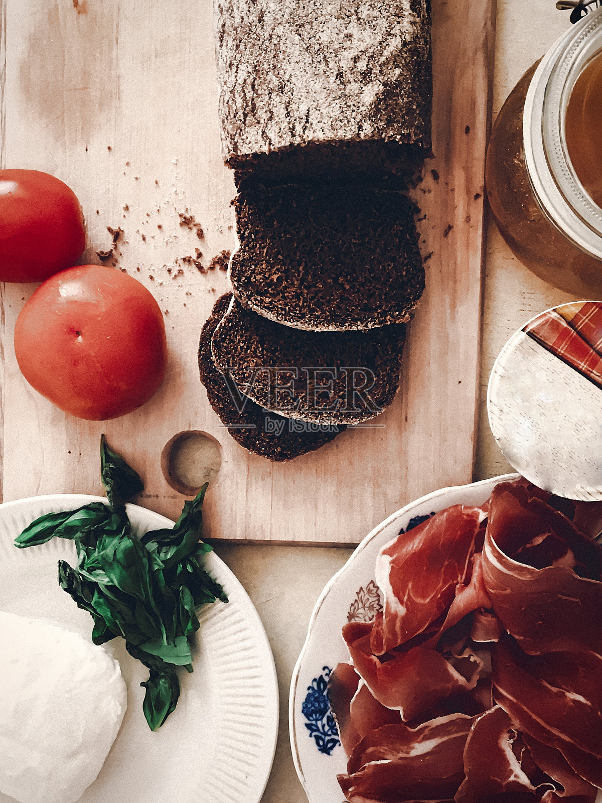 制作三明治，意大利小点心配意大利熏火腿番茄沙拉蜂蜜罗勒和酱汁，木桌和刀俯视图。空间的文本。美味的开胃菜，自制的食物照片摄影图片