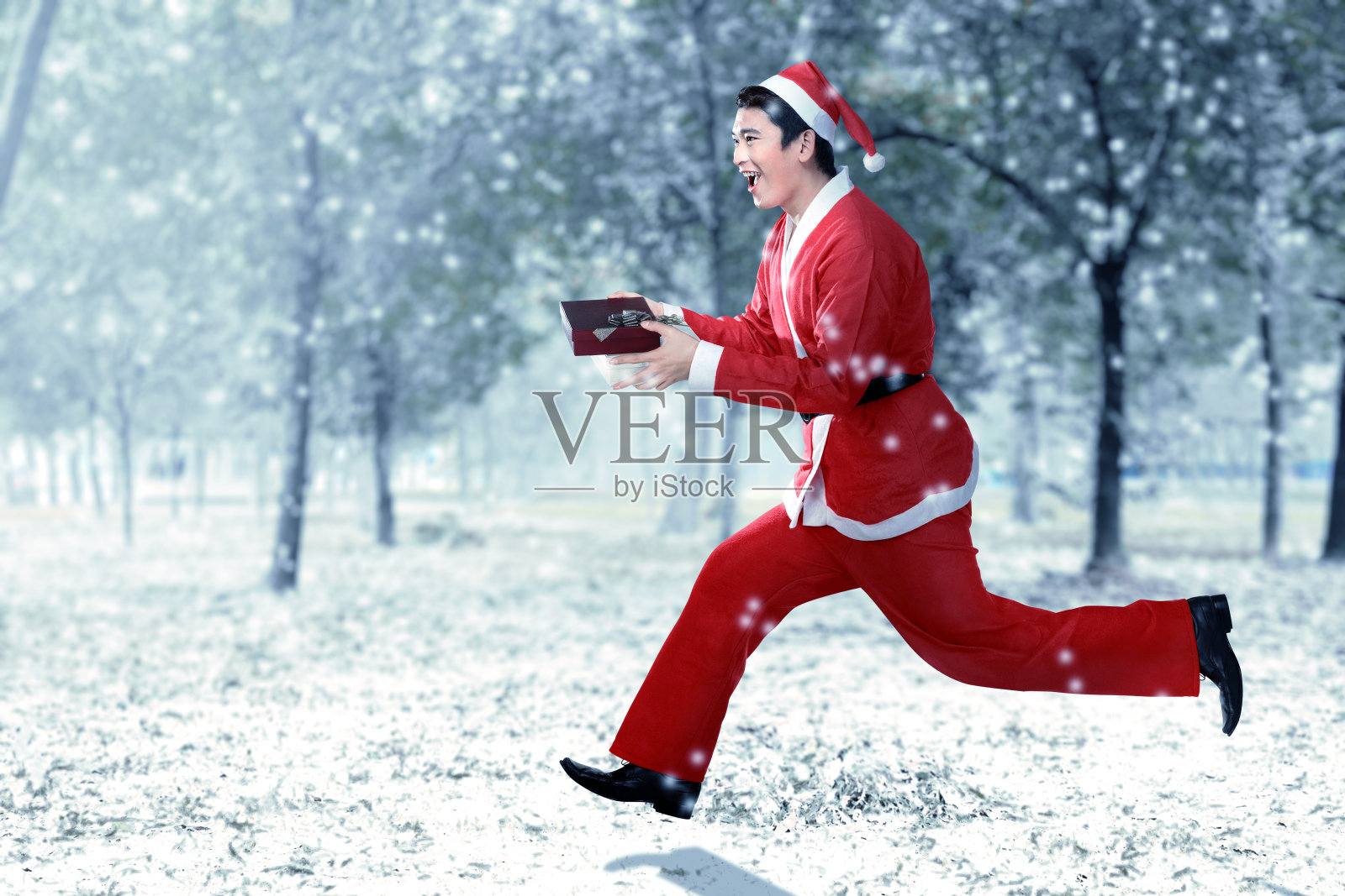 亚洲男人穿着圣诞老人服装，一边跑一边拿着礼盒照片摄影图片
