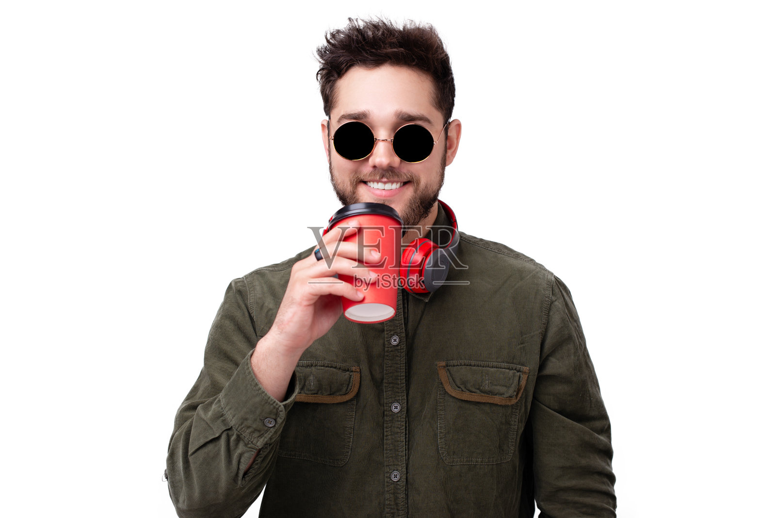 照片上的一个快乐的家伙，戴着太阳镜和耳机，拿着一个咖啡杯越过白色的墙照片摄影图片