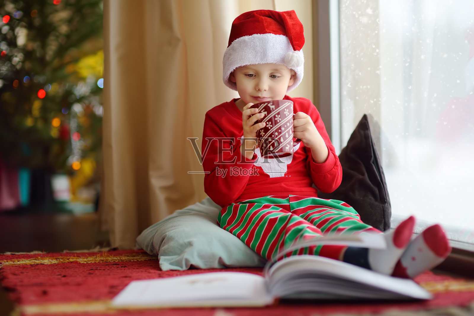 小男孩在装饰舒适的客厅里看书，喝热可可。圣诞快乐的孩子。照片摄影图片