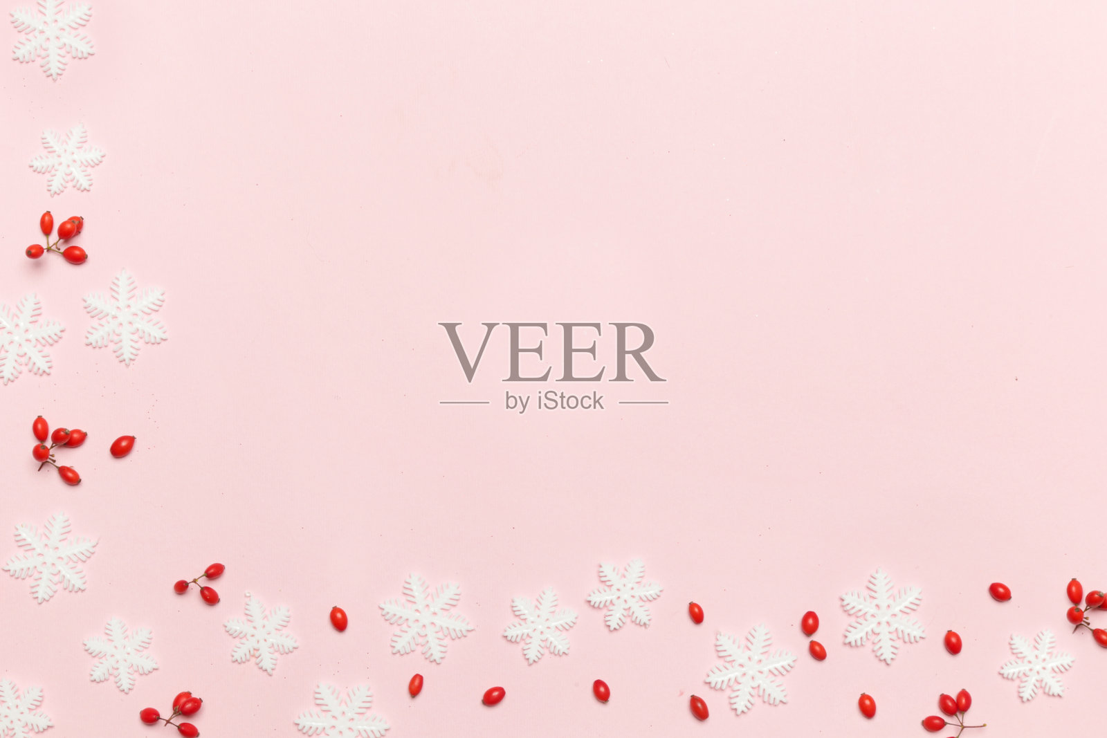 优雅的冬季背景与拷贝空间。粉红色的背景上点缀着红色的浆果和雪花。照片摄影图片