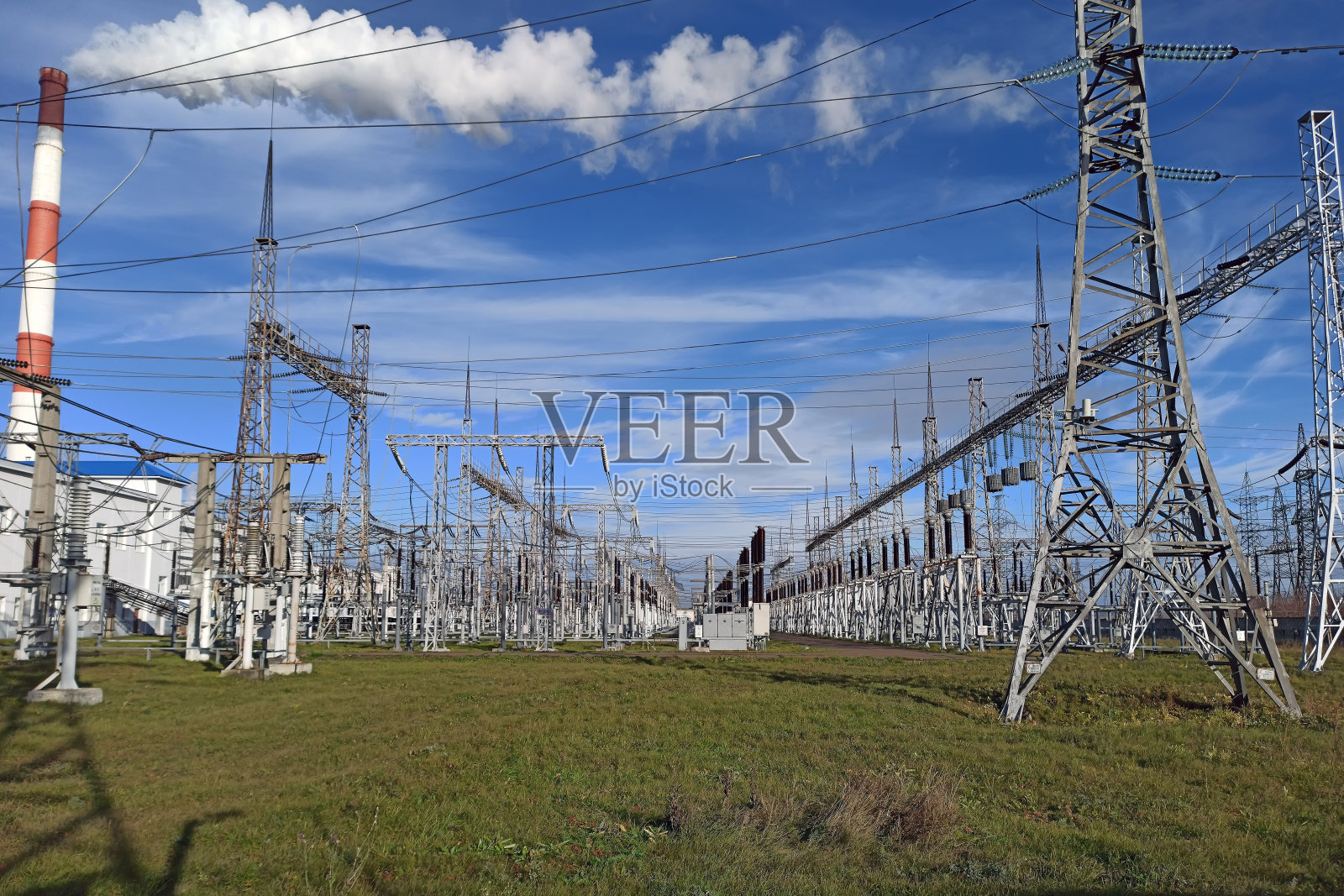 高压电塔的背景是蓝天和绿草。红色和白色的管道和来自发电厂的蒸汽。照片摄影图片