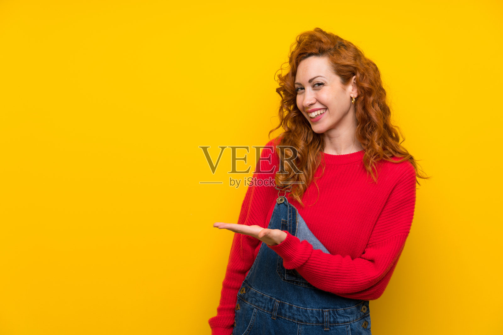 身穿工作服的红发妇女在孤立的黄色墙壁上伸出双手，邀请前来照片摄影图片