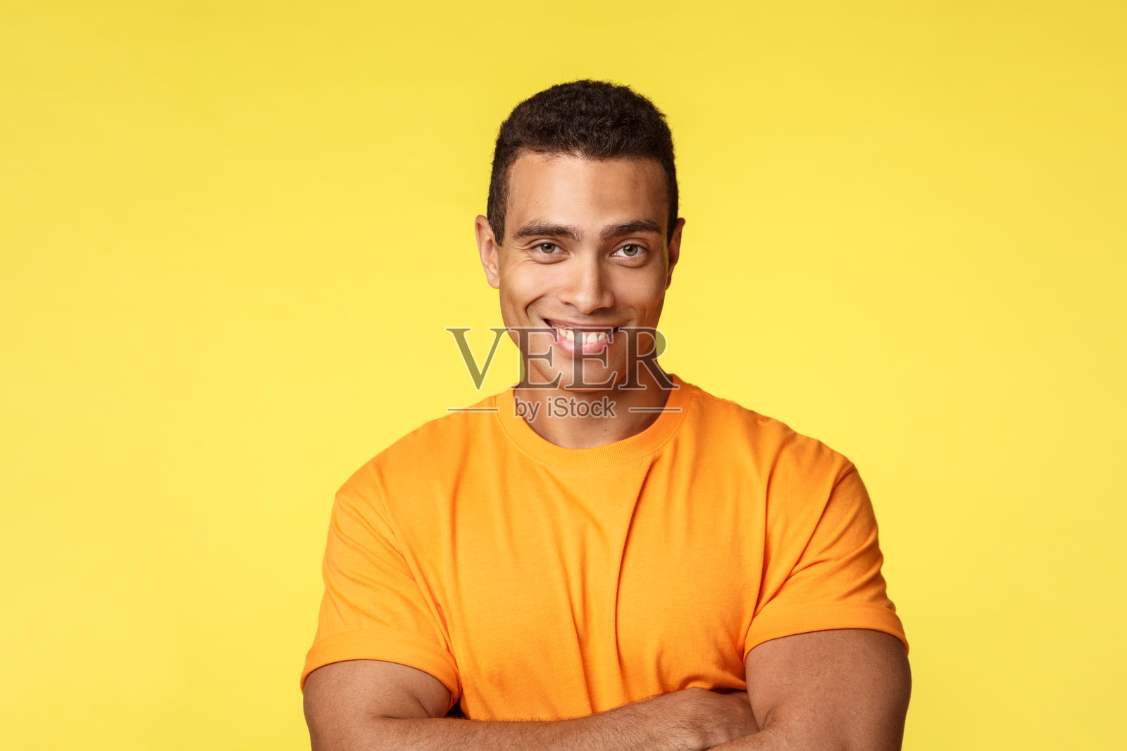 自信和厚脸皮的男子气概的t恤，交叉双臂胸部自信的姿势，微笑如毫无疑问可以赢，自信和高兴站在黄色的背景，分享有趣的新闻照片摄影图片