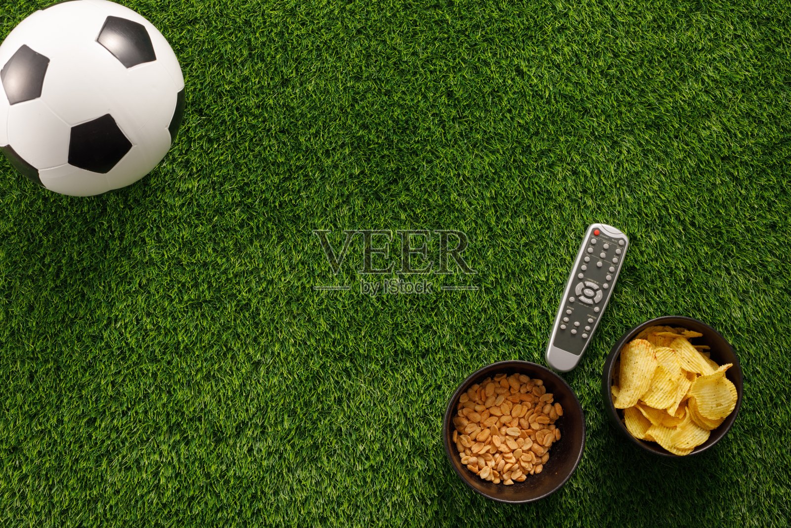 在绿色的场地上踢足球，球迷坐在长椅上吃零食，还有电视遥控器。平的。副本的空间。照片摄影图片