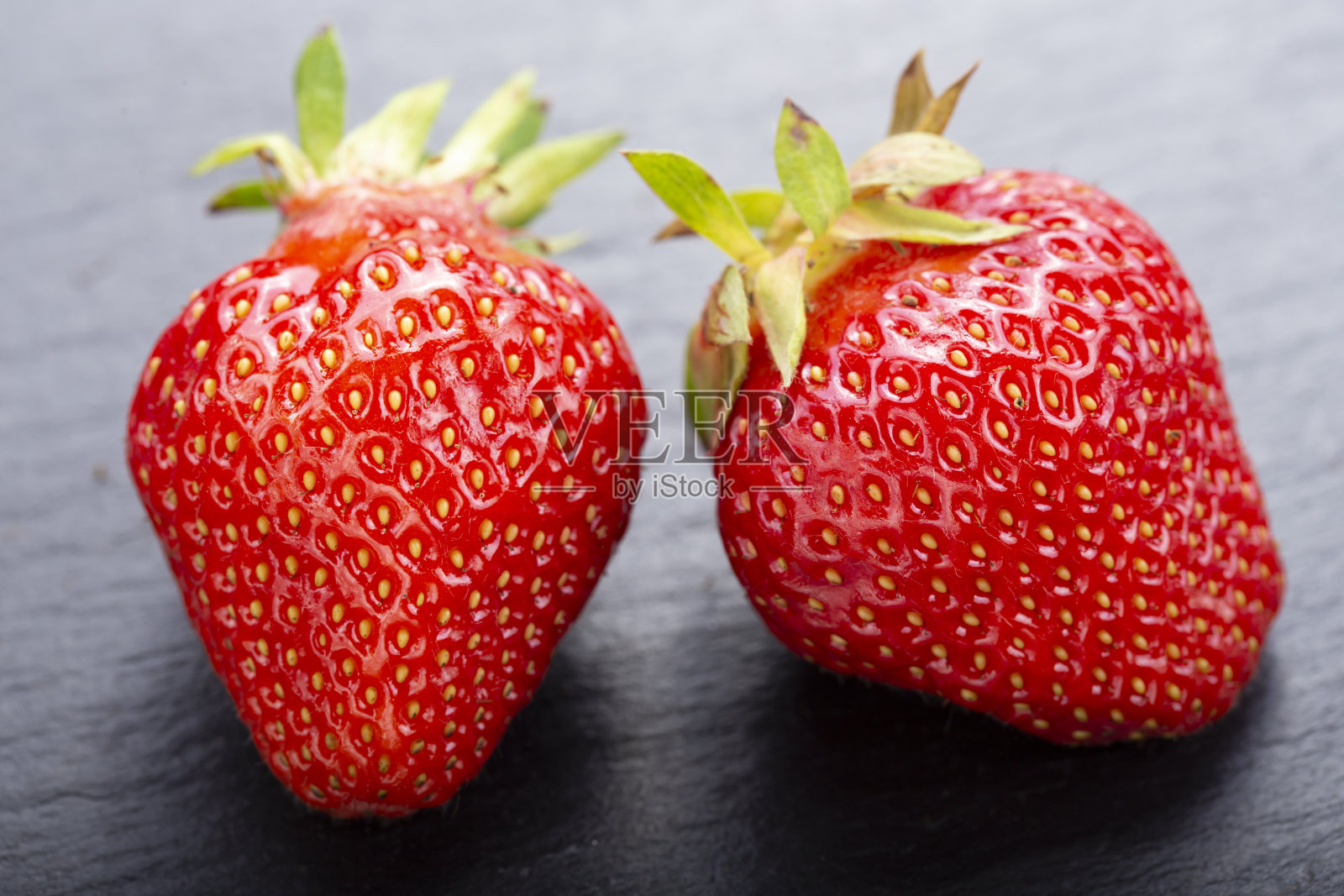 两个成熟的草莓在一个黑色的石板背景，特写。照片摄影图片