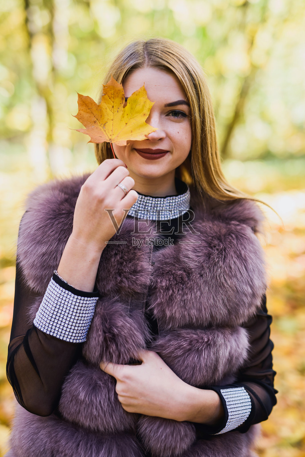时尚的女人。身着裘皮大衣的女孩微笑着出现在满是树木和常春藤的秋天公园里照片摄影图片