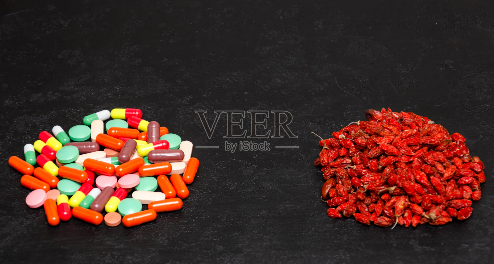 成堆的干枸杞和彩色的胶囊在黑色的背景。传统医学与替代医学概念。健康超级食物vs传统药物。特写镜头。本空间照片摄影图片