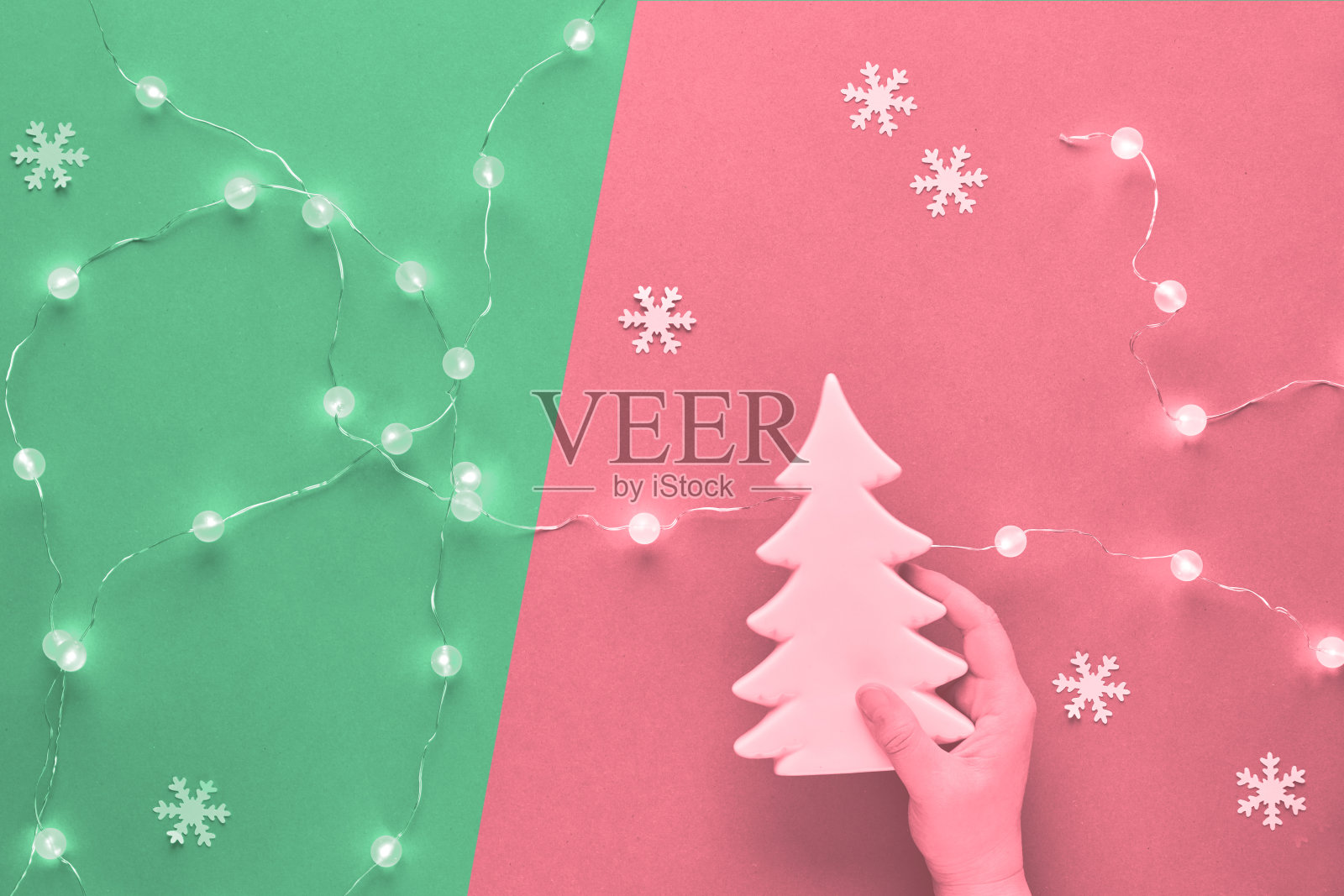 冬季节日构图，单色图像调成两种色调，粉色和新薄荷绿。手握陶瓷杉木装饰。新年或圣诞节平躺着雪花。照片摄影图片