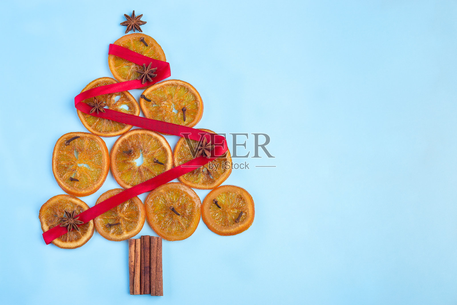 圣诞树由橙色糖果片、肉桂棒、八角星和丁香制成，用红丝带装饰，在蓝色背景上，水平，顶视图，复制空间照片摄影图片