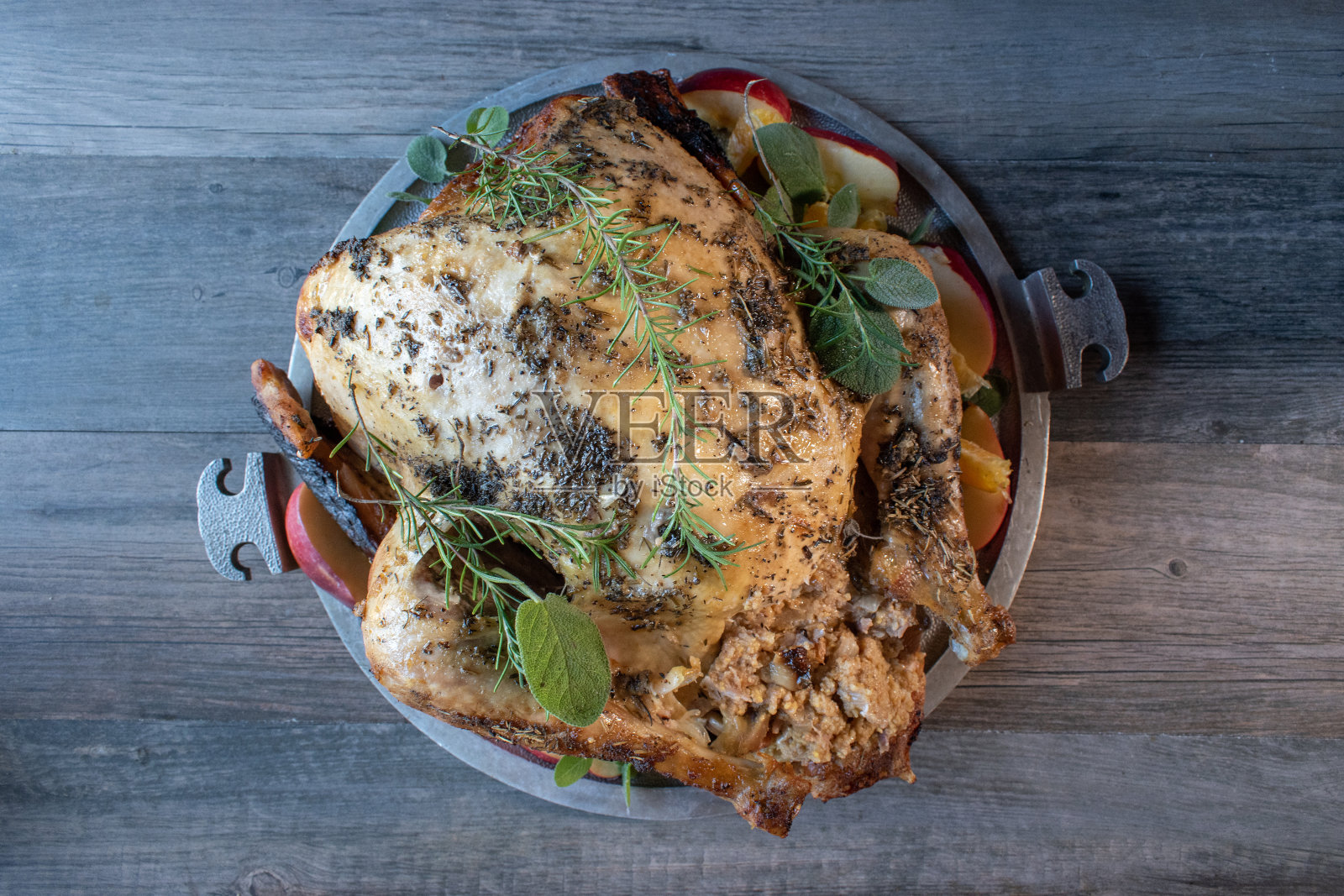 用迷迭香和鼠尾草装饰的圆形托盘配以整只烤香草火鸡照片摄影图片