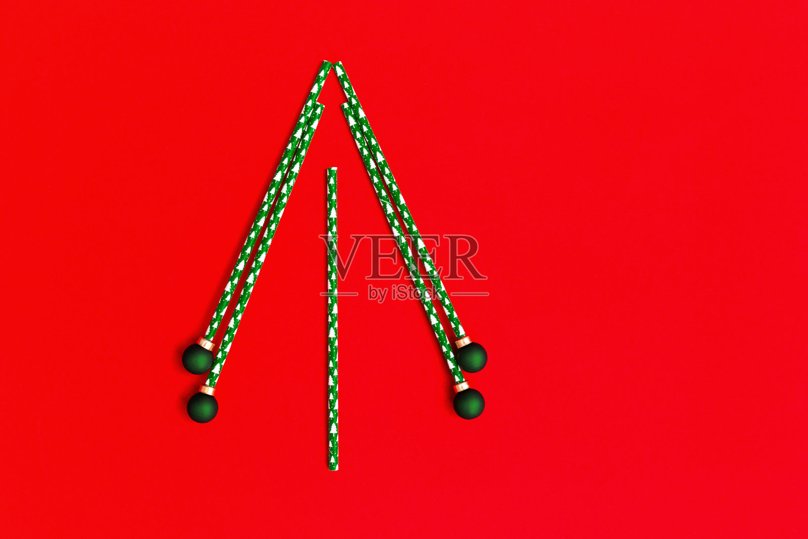 红色背景下的吸管和绿色新年球的创意圣诞树。假日冬季概念与明亮的颜色。最小平。照片摄影图片