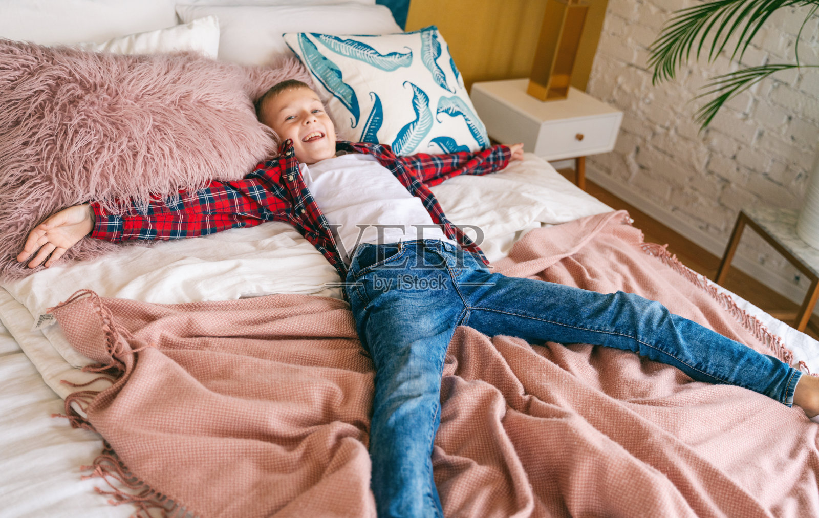 快乐快乐的8岁小男孩躺在自己房间的床上，假期游手好闲的概念照片摄影图片