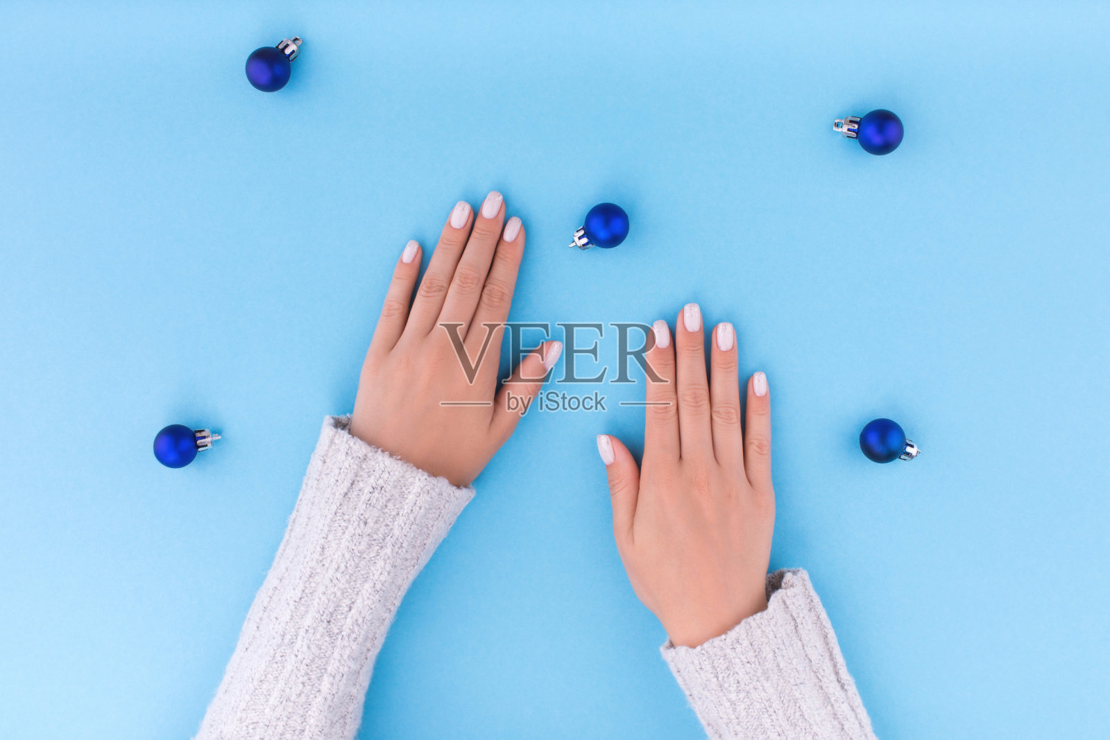 美丽的年轻女人的手与美甲在蓝色的背景与圣诞球。照片摄影图片
