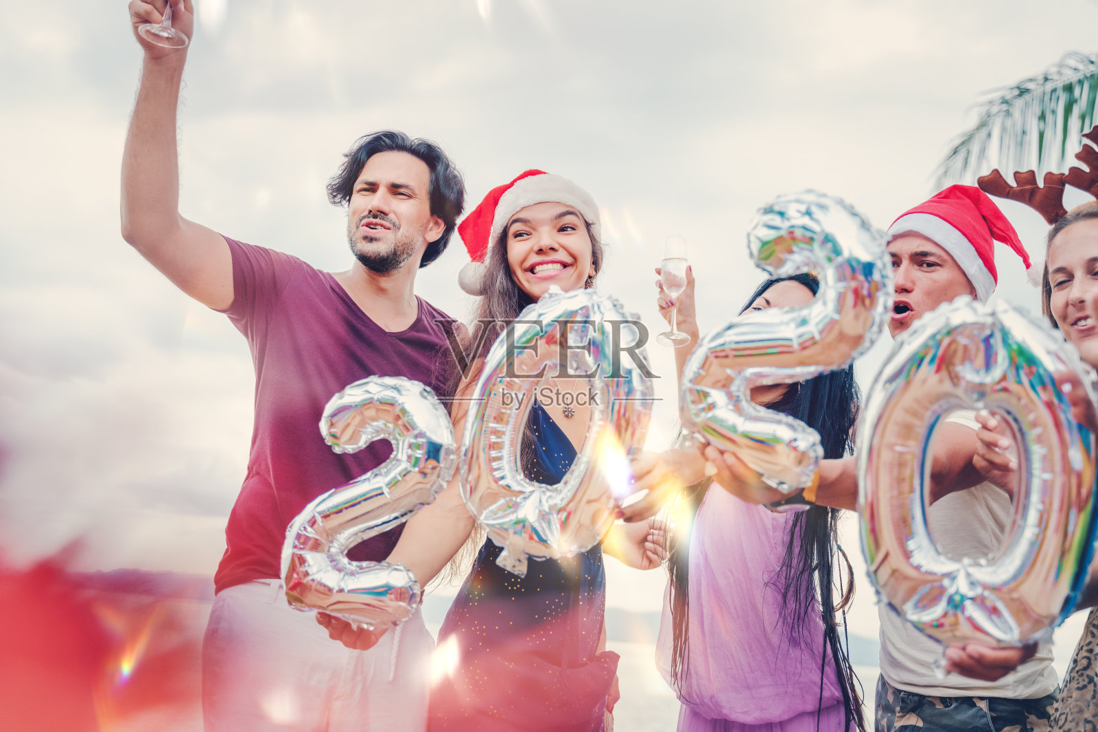 在一个热带度假胜地，一群快乐的混血儿手里拿着数字庆祝圣诞和新年。照片摄影图片