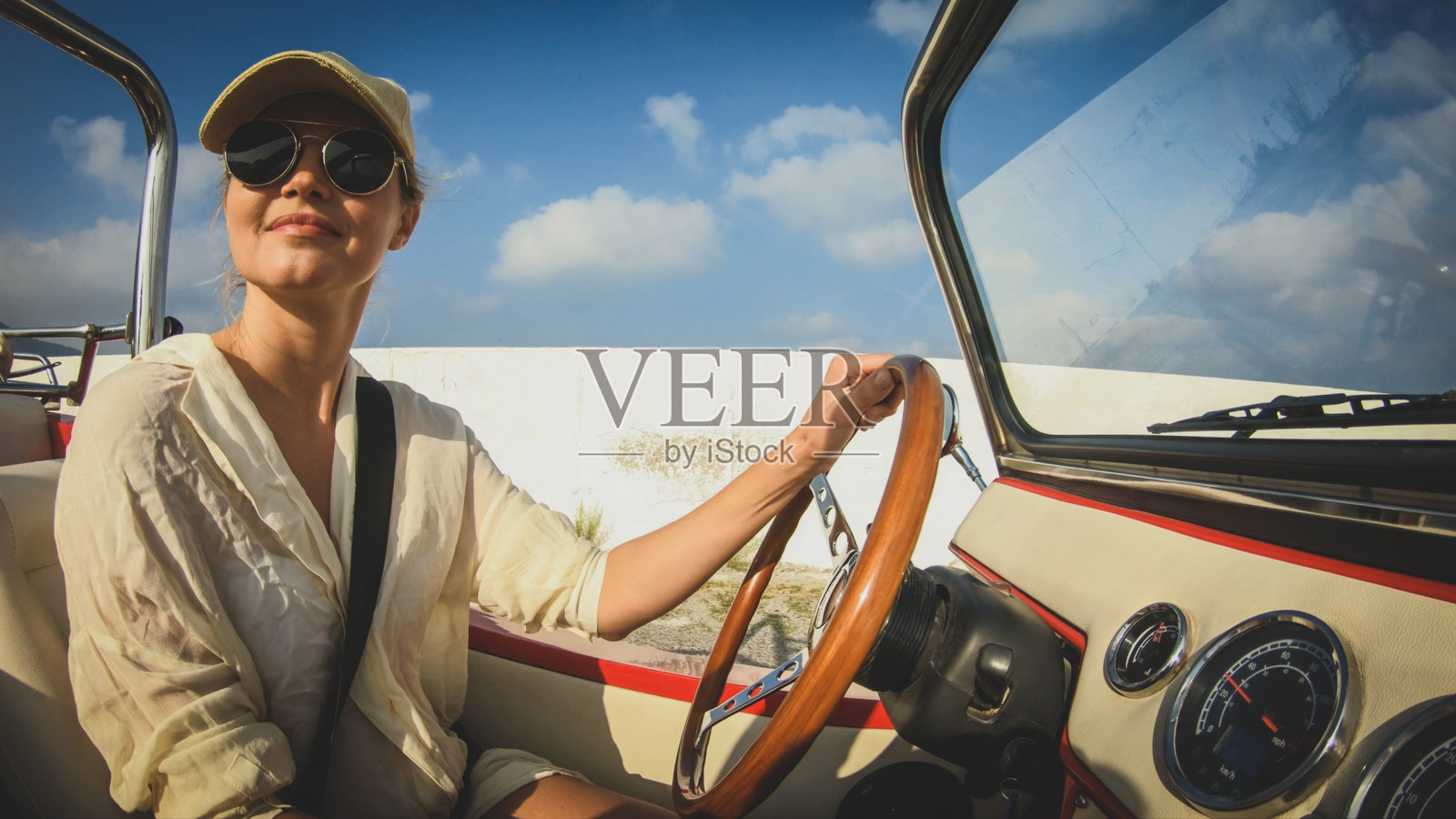 微笑的女人戴着太阳镜，金发，开着一辆没有屋顶的车照片摄影图片