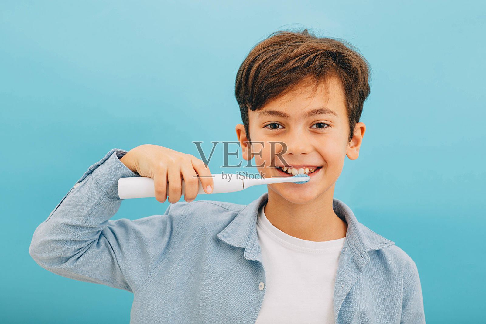 混血小男孩清洁牙齿与声波牙刷在蓝色背景。用酷酷的牙刷完美去除牙菌斑照片摄影图片
