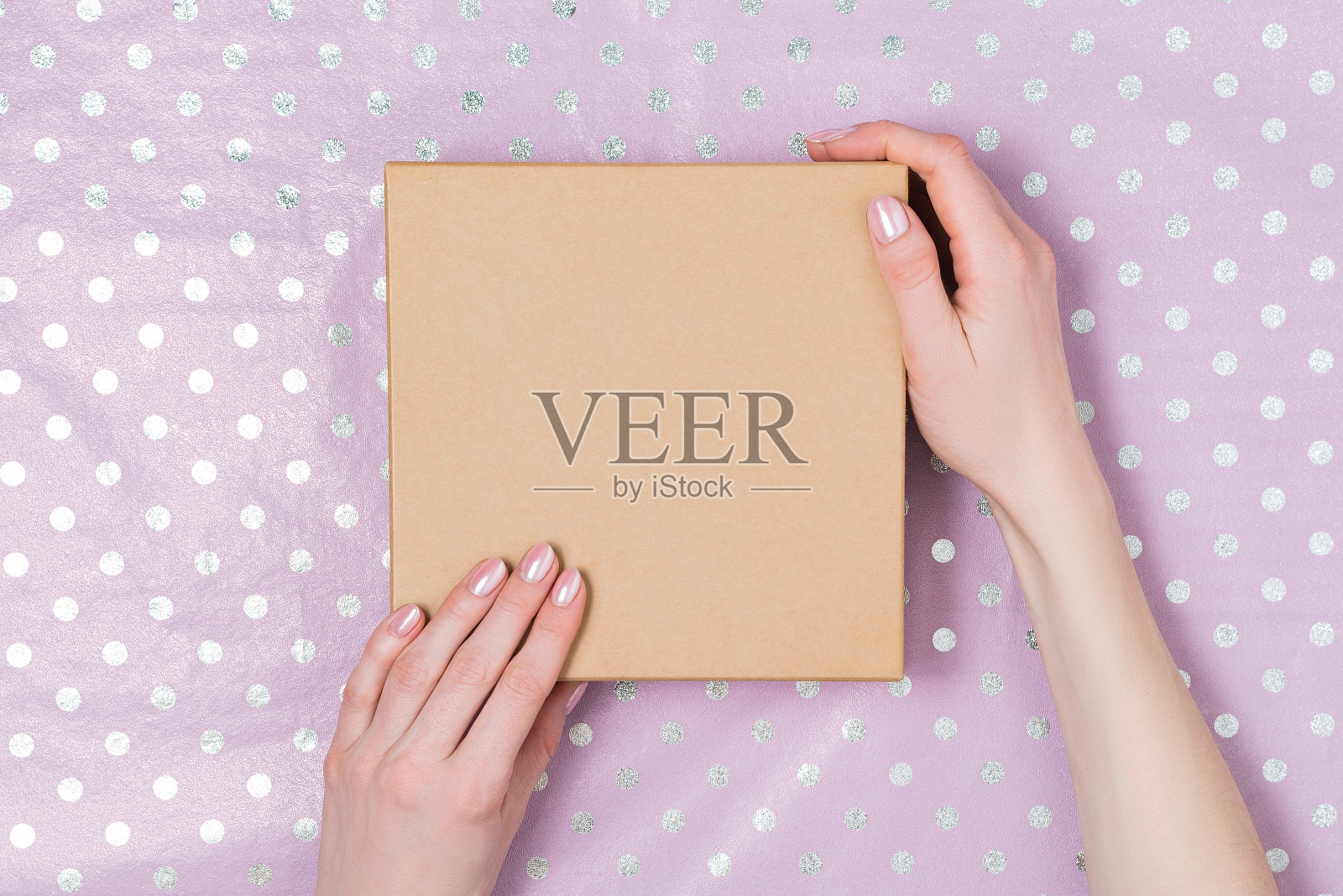 女人手里拿着纸板箱。丁香圆点背景。微妙的粉红色指甲。照片摄影图片