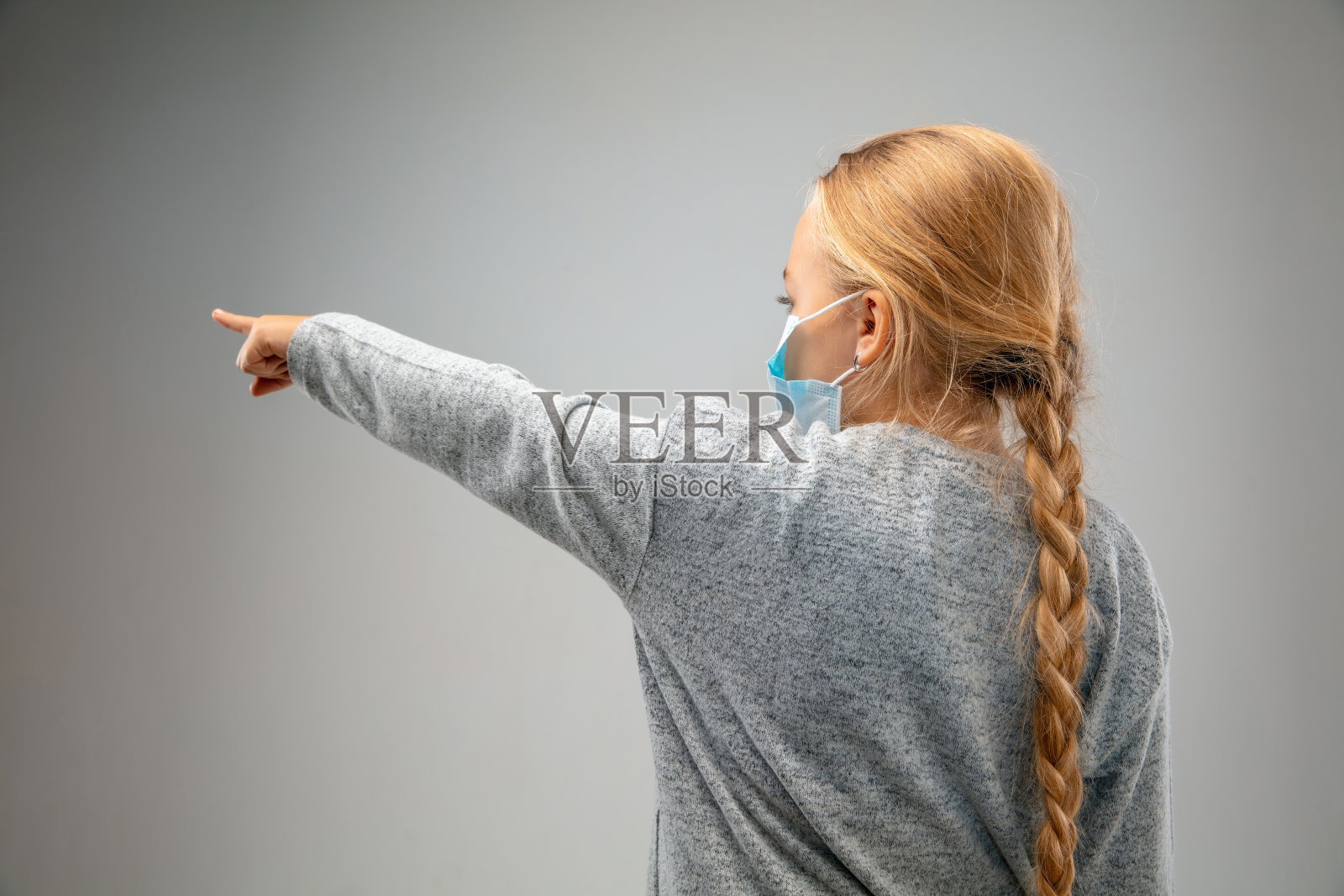 白色的女孩戴着呼吸保护口罩，以防止空气污染和黄昏在灰色的工作室背景照片摄影图片