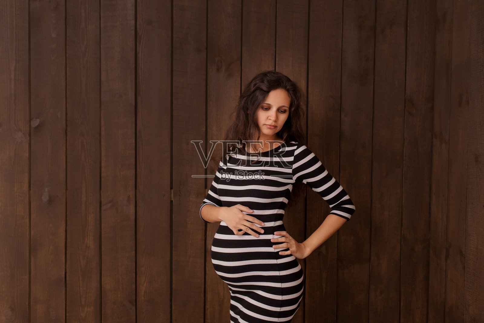 身穿条纹裙的孕妇双手放在深棕色的腹部上。怀孕、分娩、准备和期望概念。美丽柔情的怀孕照片照片摄影图片