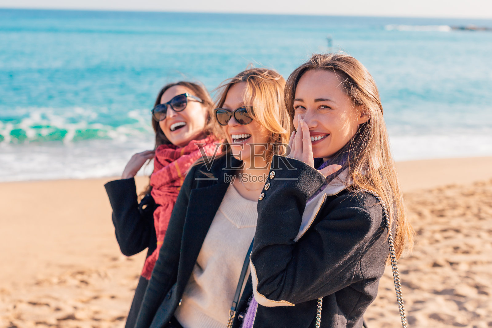 快乐美丽的女孩有乐趣的冬季海滩(巴塞罗那，西班牙)-三个女人朋友一起笑-女性友谊的概念照片摄影图片