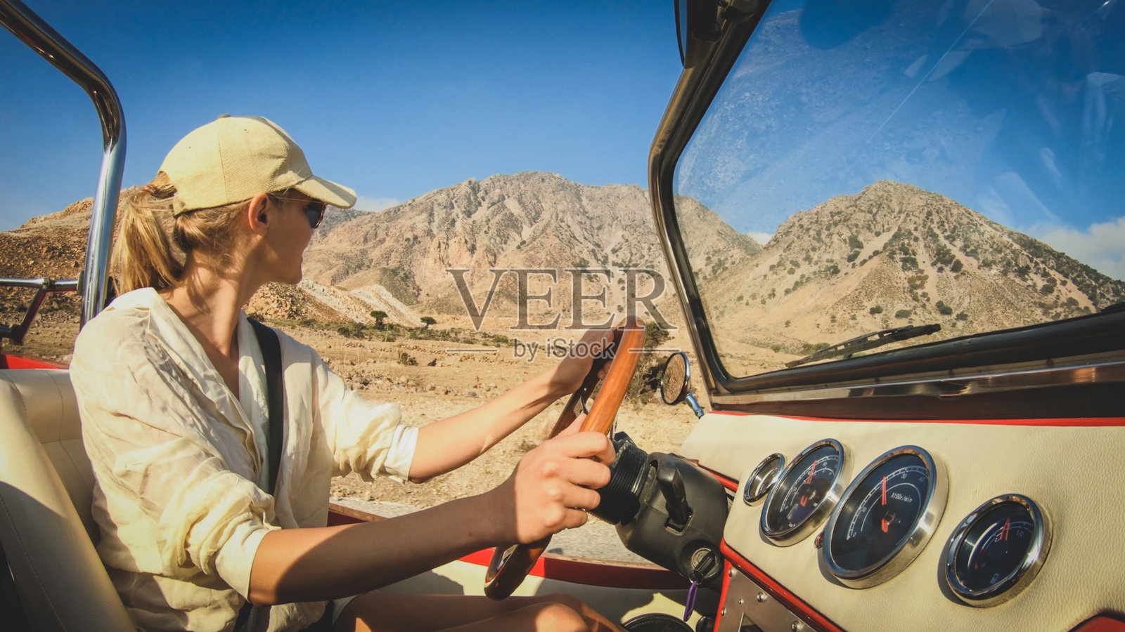 一个戴着墨镜金发的女人开着一辆没有屋顶的车。背景是尼斯罗斯火山。照片摄影图片