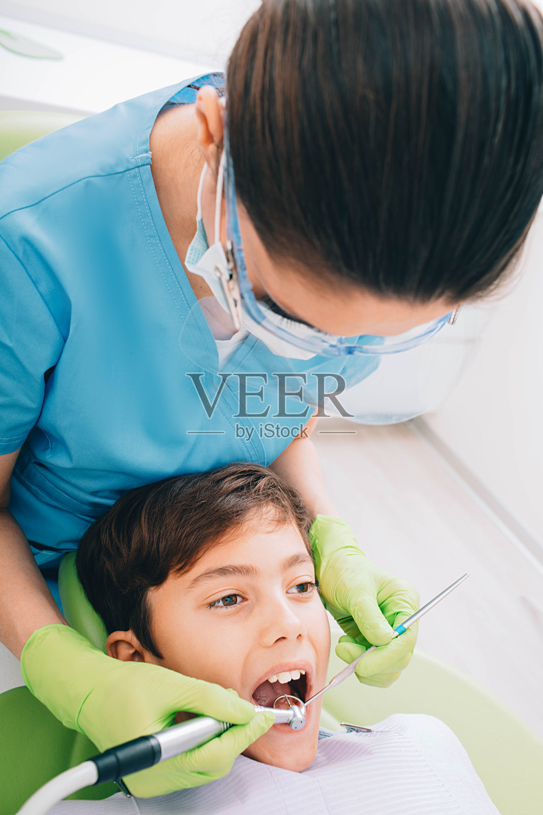 牙科医生在诊所用牙钻给一个小男孩做牙齿治疗照片摄影图片