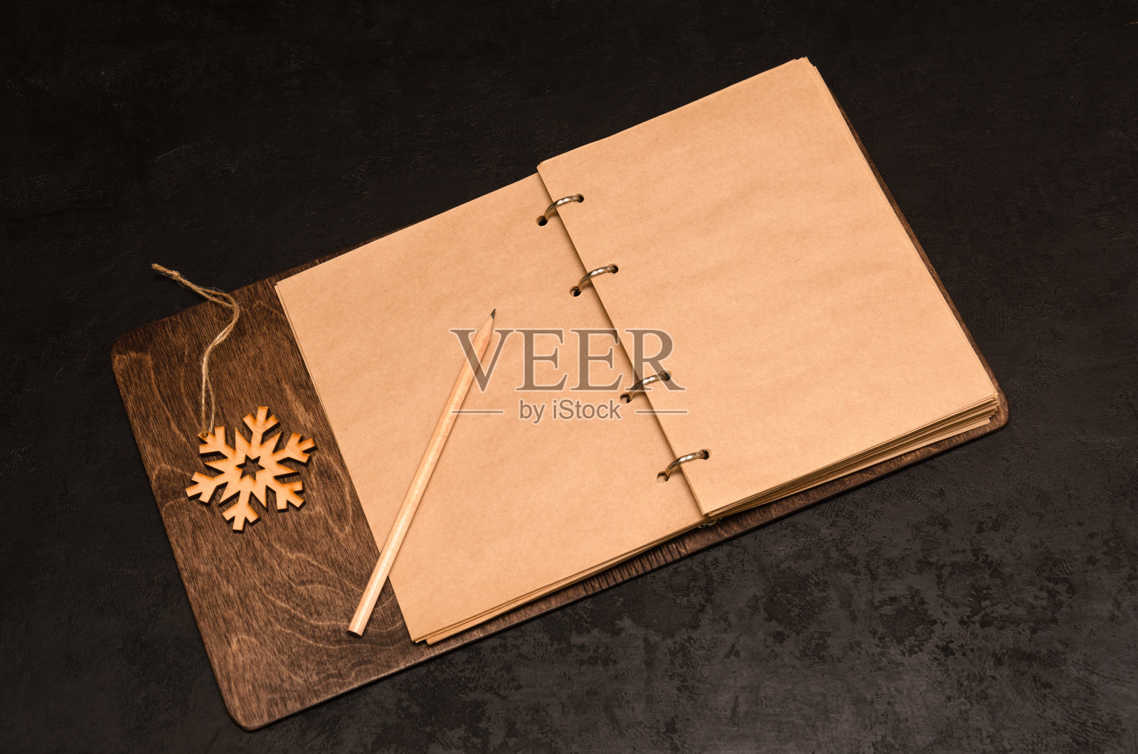 牛皮纸笔记本与空白纸在一个木制封面与拷贝空间，铅笔和木制雪花在黑色的背景照片摄影图片