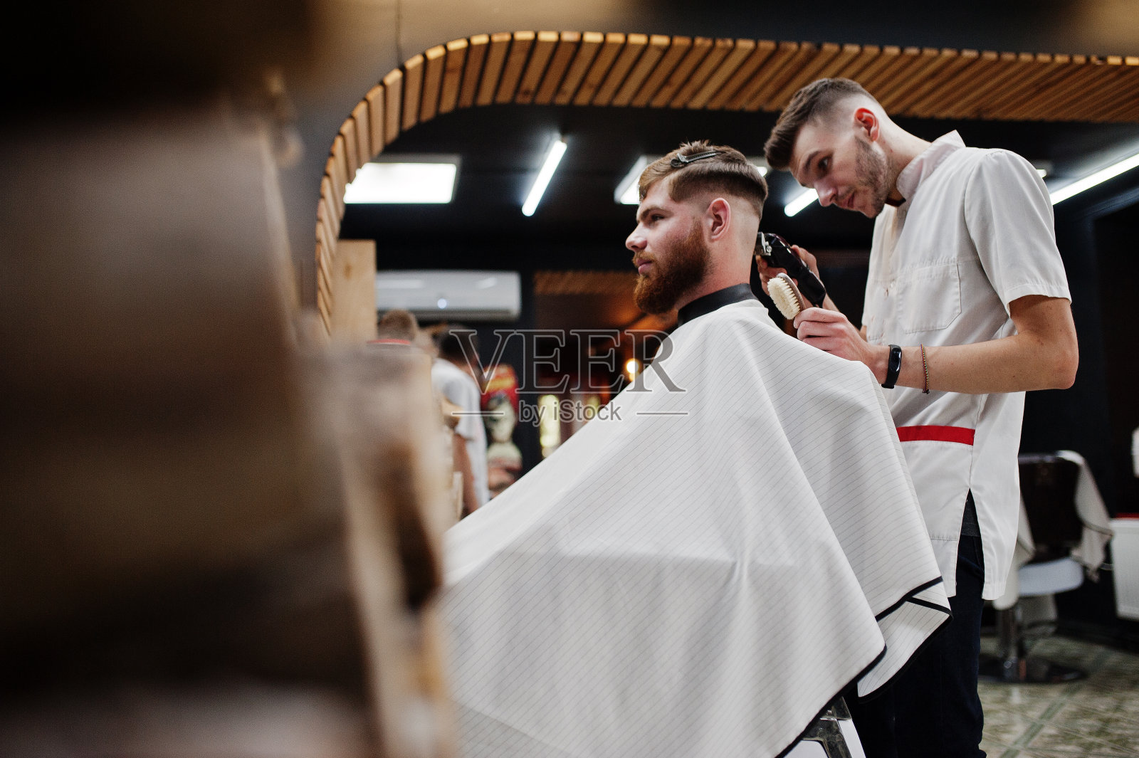 一个留着胡子的年轻人坐在理发店的椅子上理发。理发师的灵魂。照片摄影图片