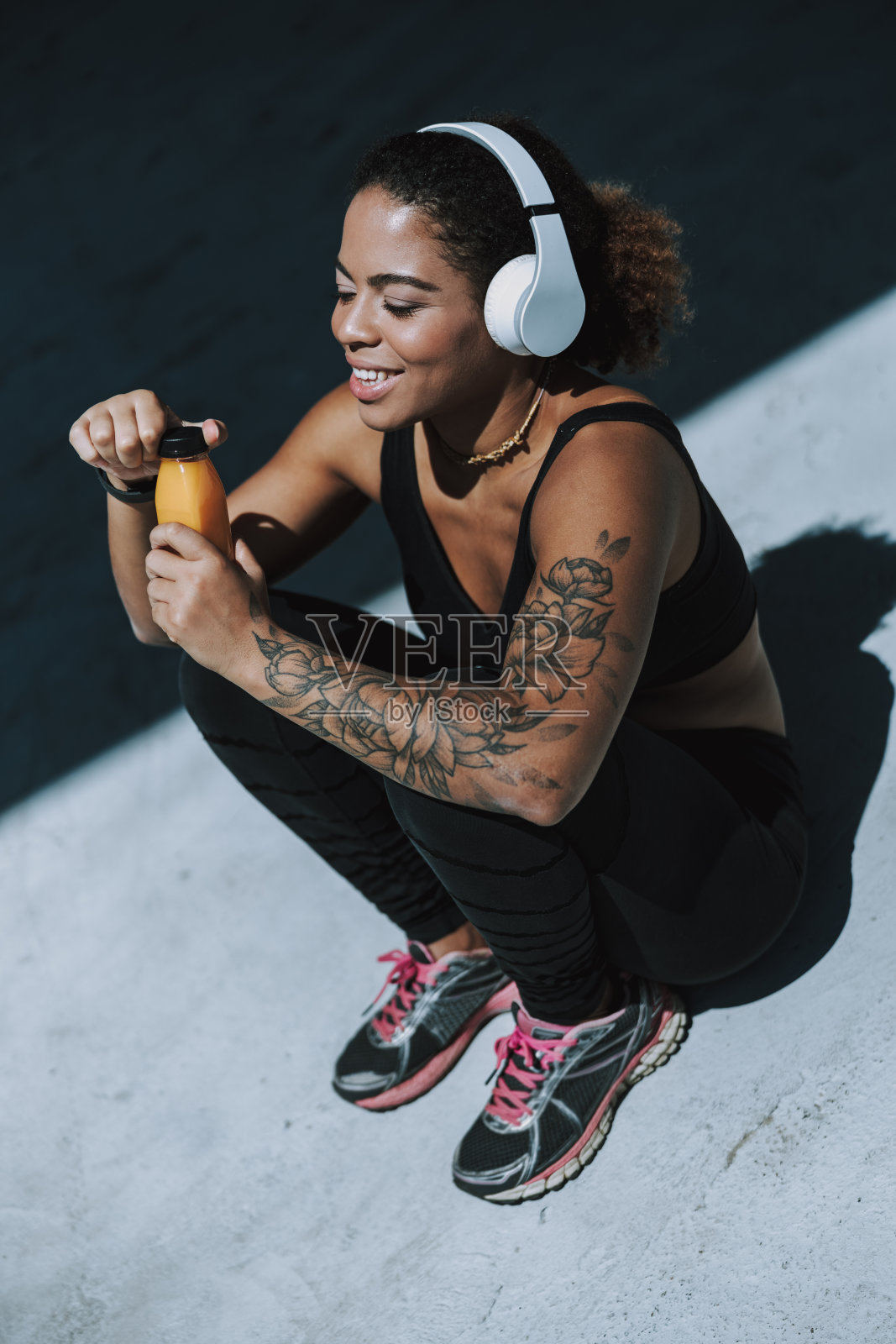 微笑的非洲裔美国女士戴着耳机拿着一瓶果汁照片摄影图片