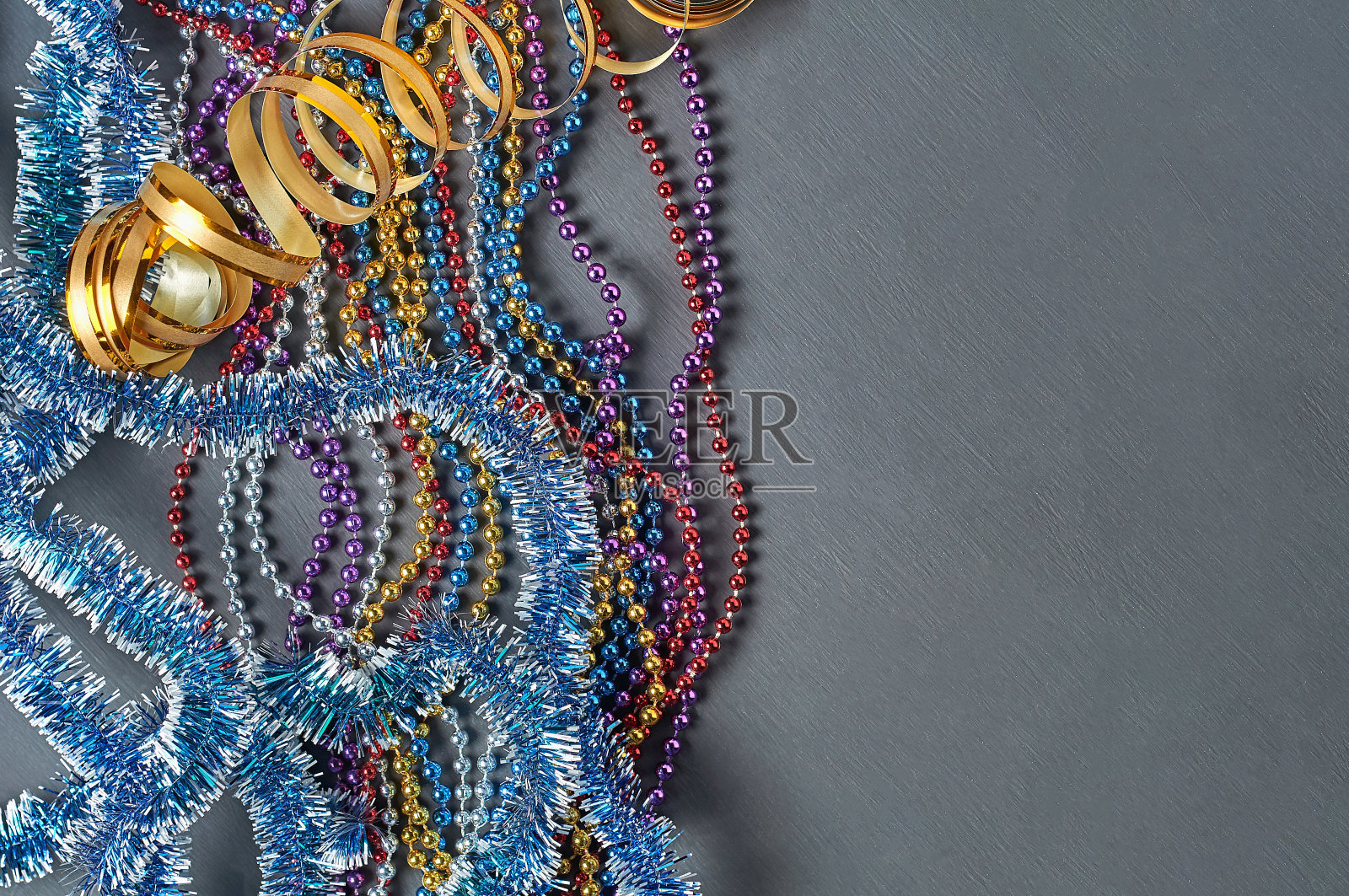 蓝色的金属丝，金色的缎带和不同颜色的长珠子躺在深色的粗糙的混凝土桌上。空间的文本。俯视图照片摄影图片