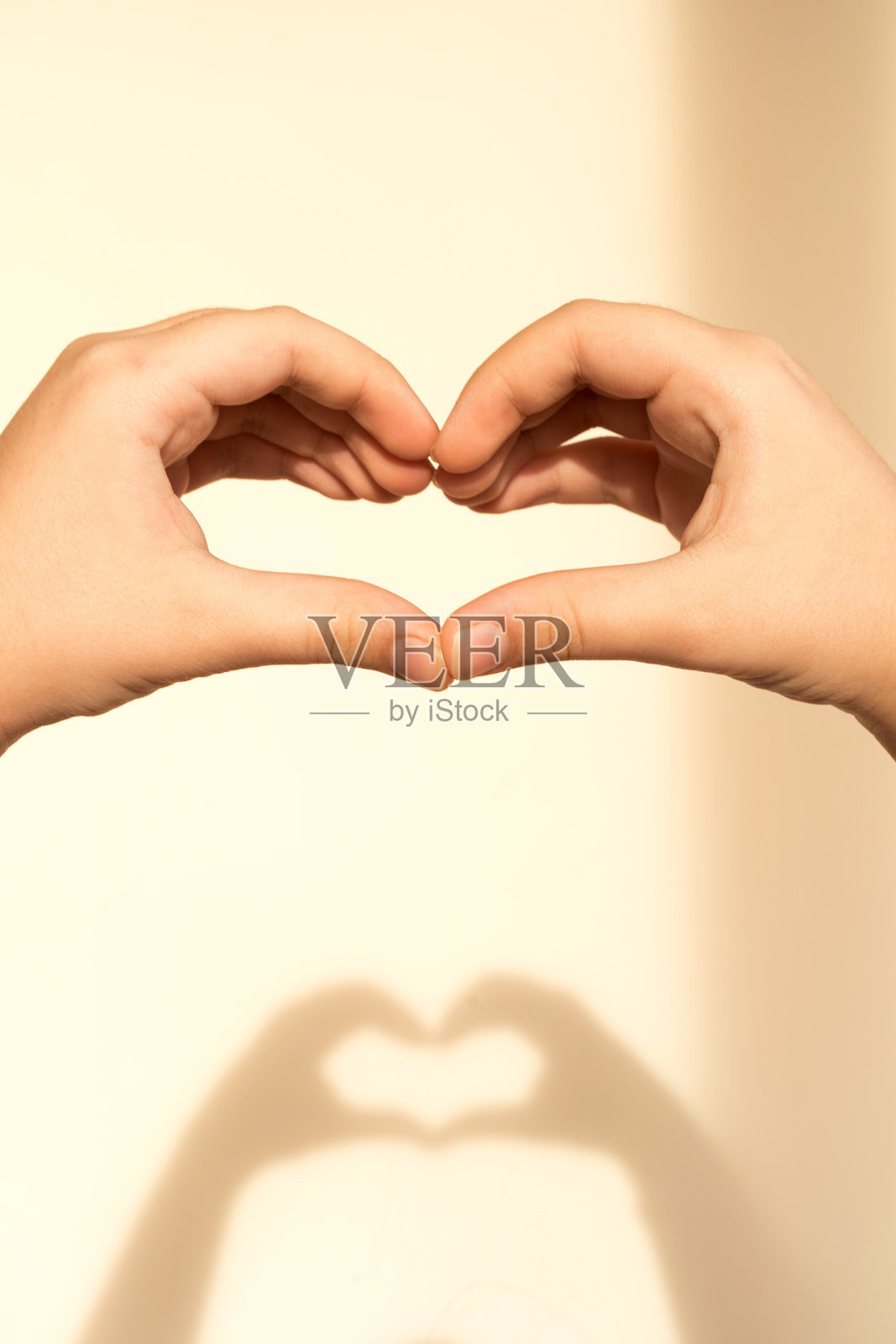 一个十几岁的女孩的手折叠成一个心的形状，从他们的影子在浅褐色的墙上照片摄影图片