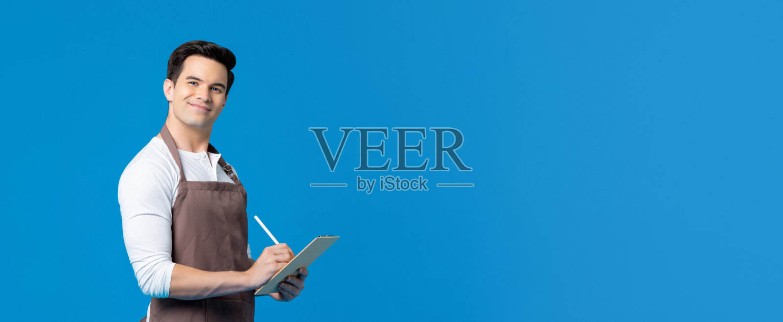 帅气的咖啡师穿着围裙在写字板上写订单照片摄影图片